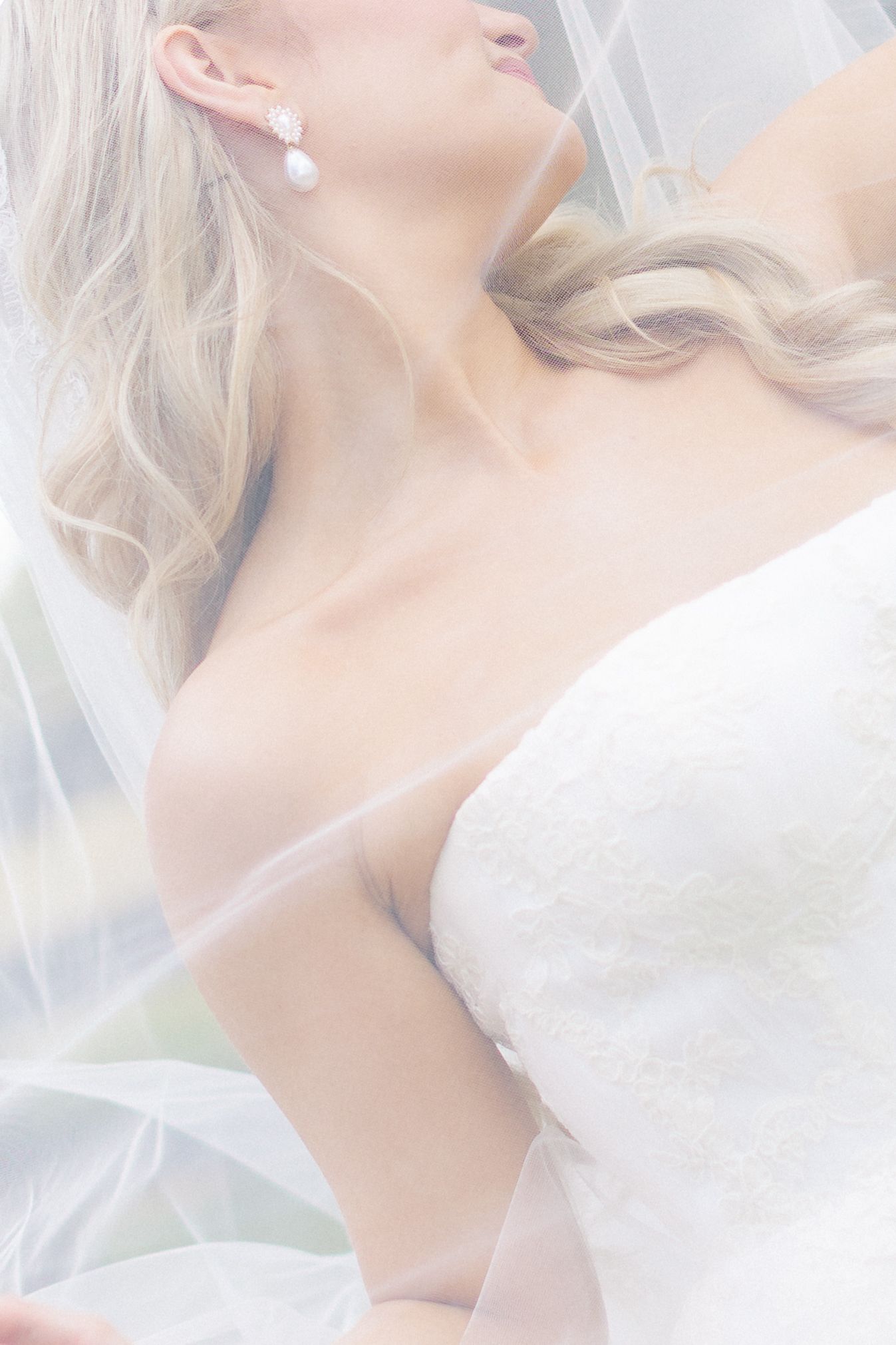 Bride in strapless white lace wedding dress with veil and pearl drop earrings, blonde hair styled in soft waves, wedding at Bella Cosa