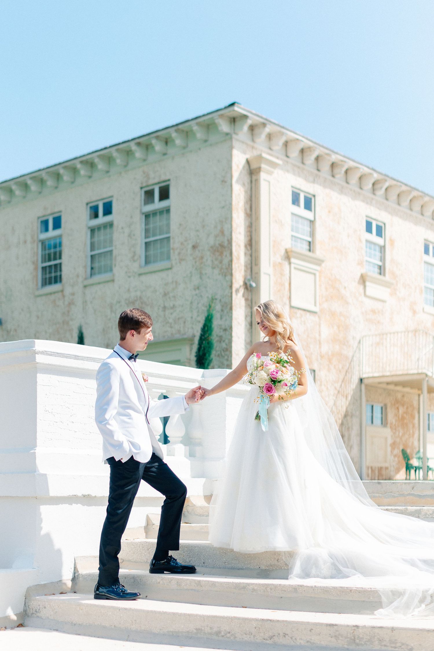 Bride and groom holding hands on white steps outside a historic building on their wedding day, wedding at Bella Cosa