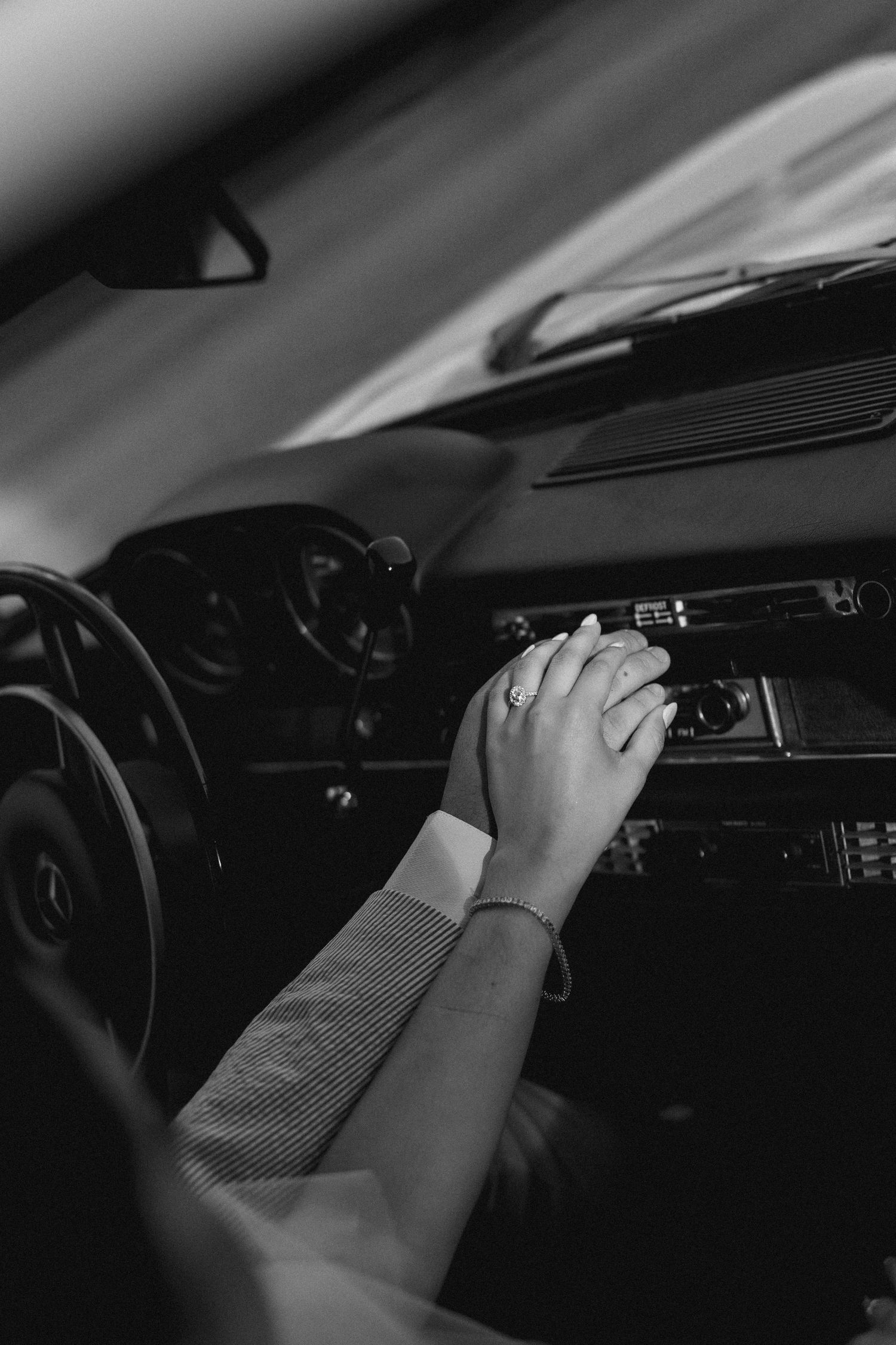 Black and white photo of a couple holding hands inside a vintage Mercedes-Benz car on their wedding day.