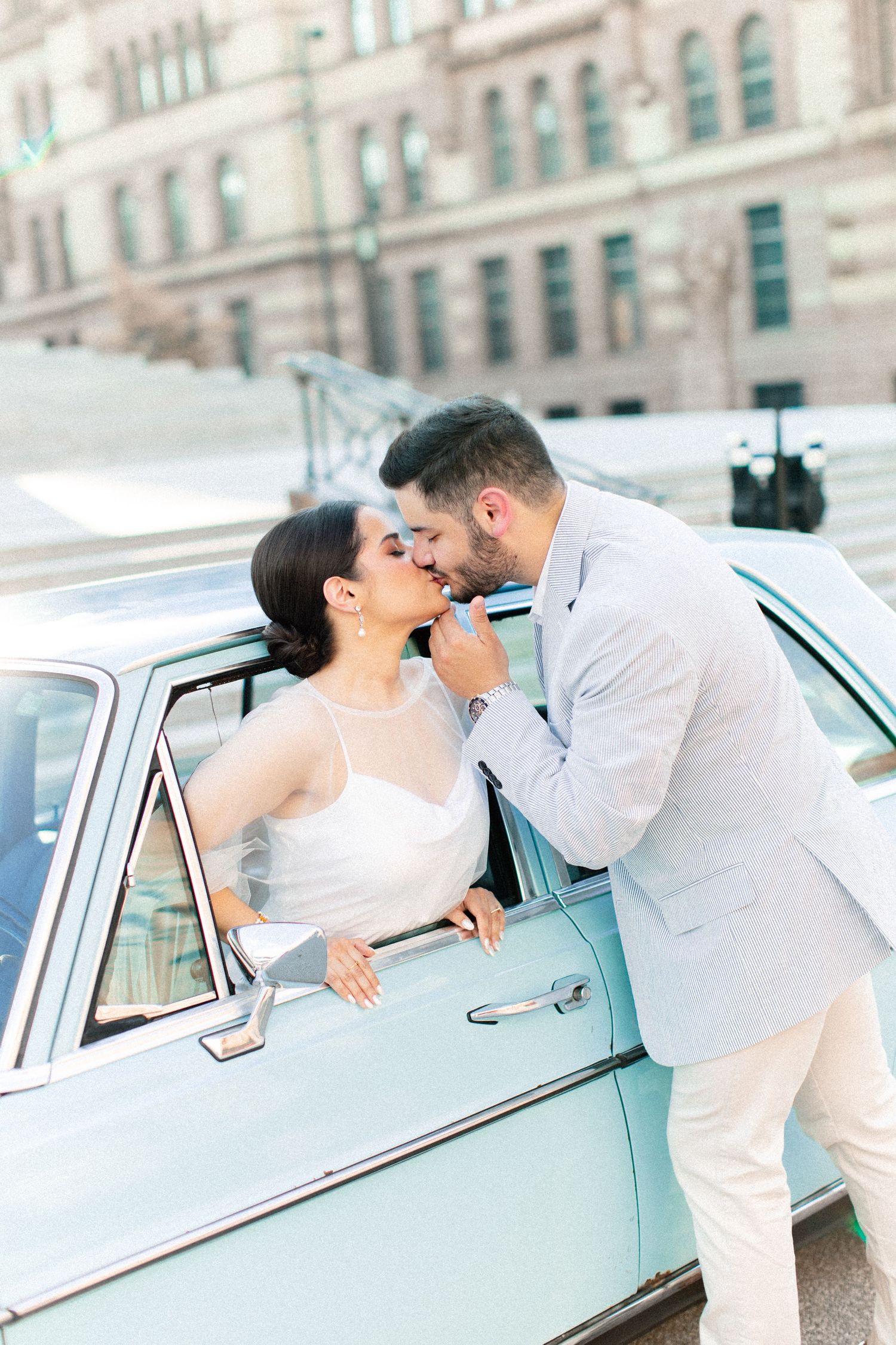 Bride and groom share a romantic kiss beside a vintage mint green car on their wedding day.