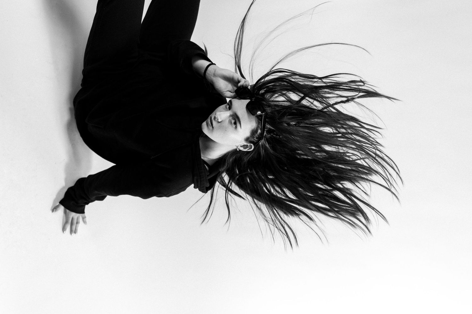 Black and white photo of a woman with long flowing hair, wearing black, captured from above in a dramatic pose.