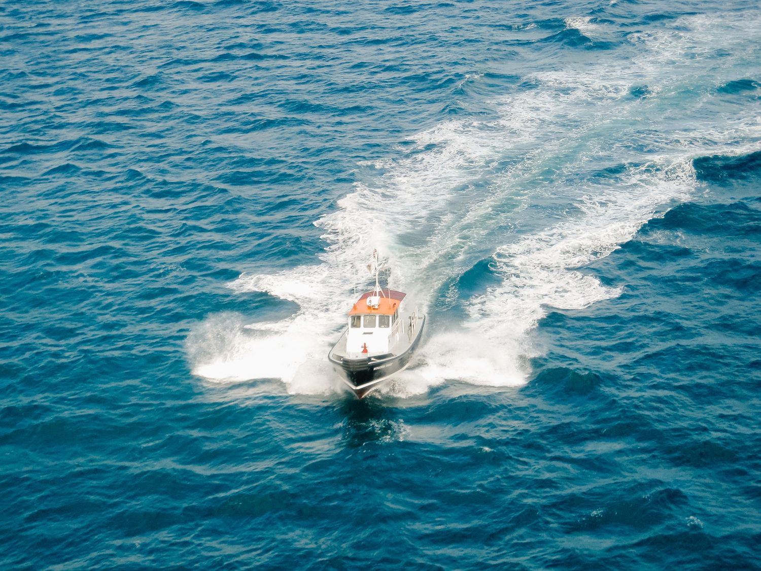Aerial view of a white and orange speedboat cutting through vivid turquoise ocean water leaving a white wake.