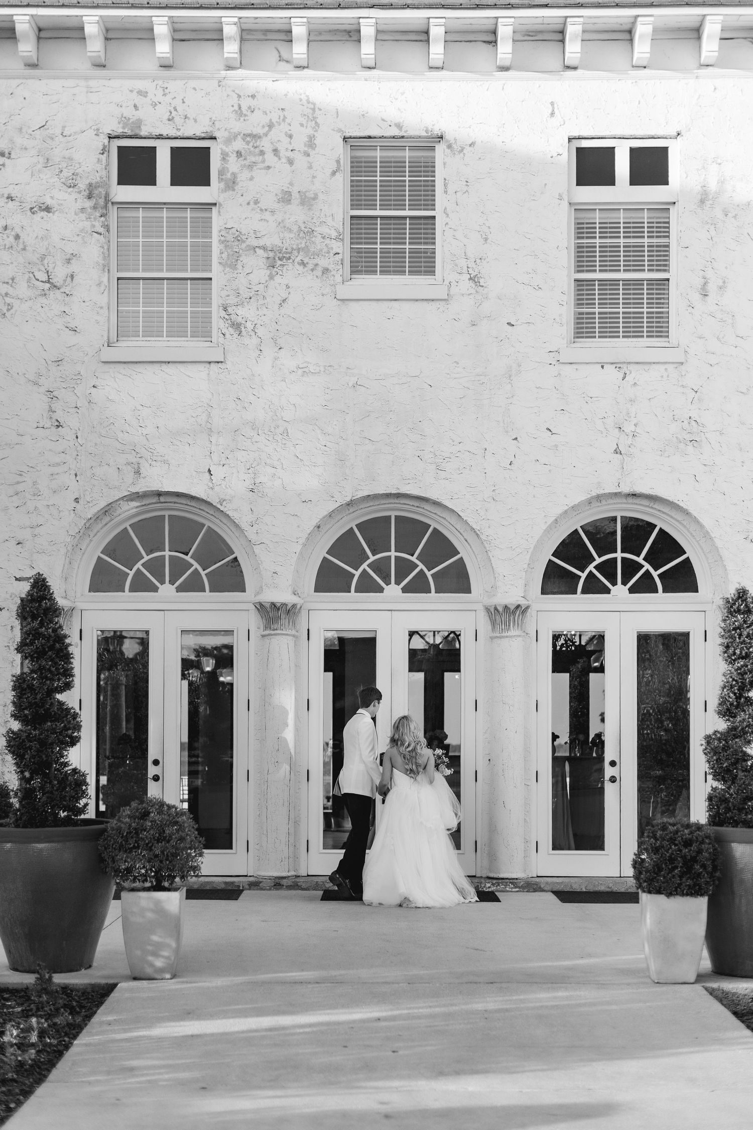 Black and white photo of a bride and groom sharing a romantic moment outside an elegant building with arched French doors, Florida