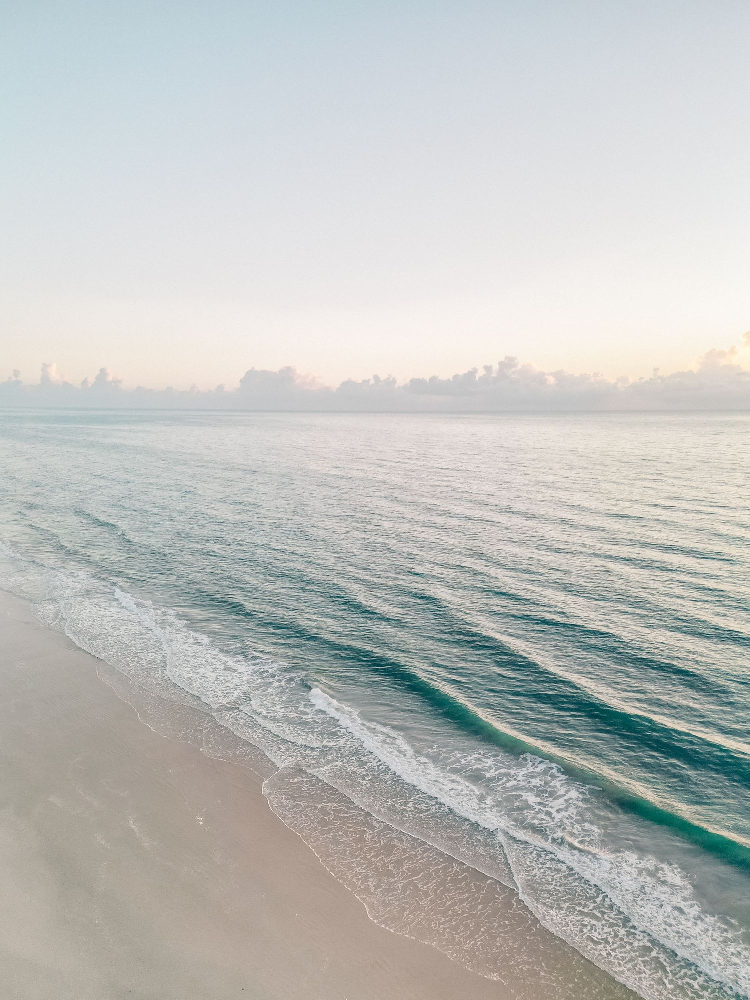 Serene tropical beach at sunrise with turquoise waves gently washing ashore under a soft pastel sky.