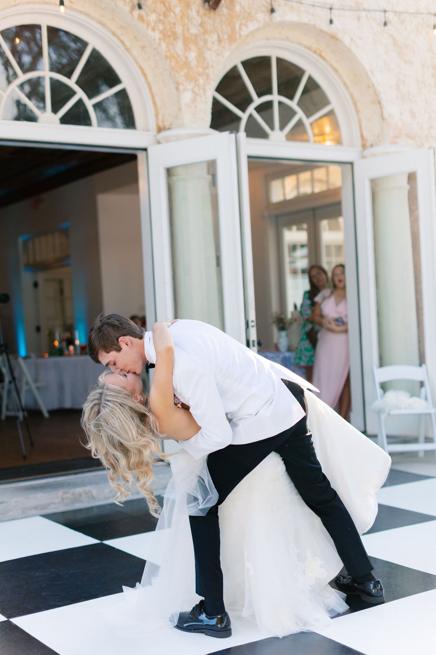 Bride and groom share a romantic dip kiss on a black and white checkered dance floor at their wedding reception, wedding at Bella Cosa