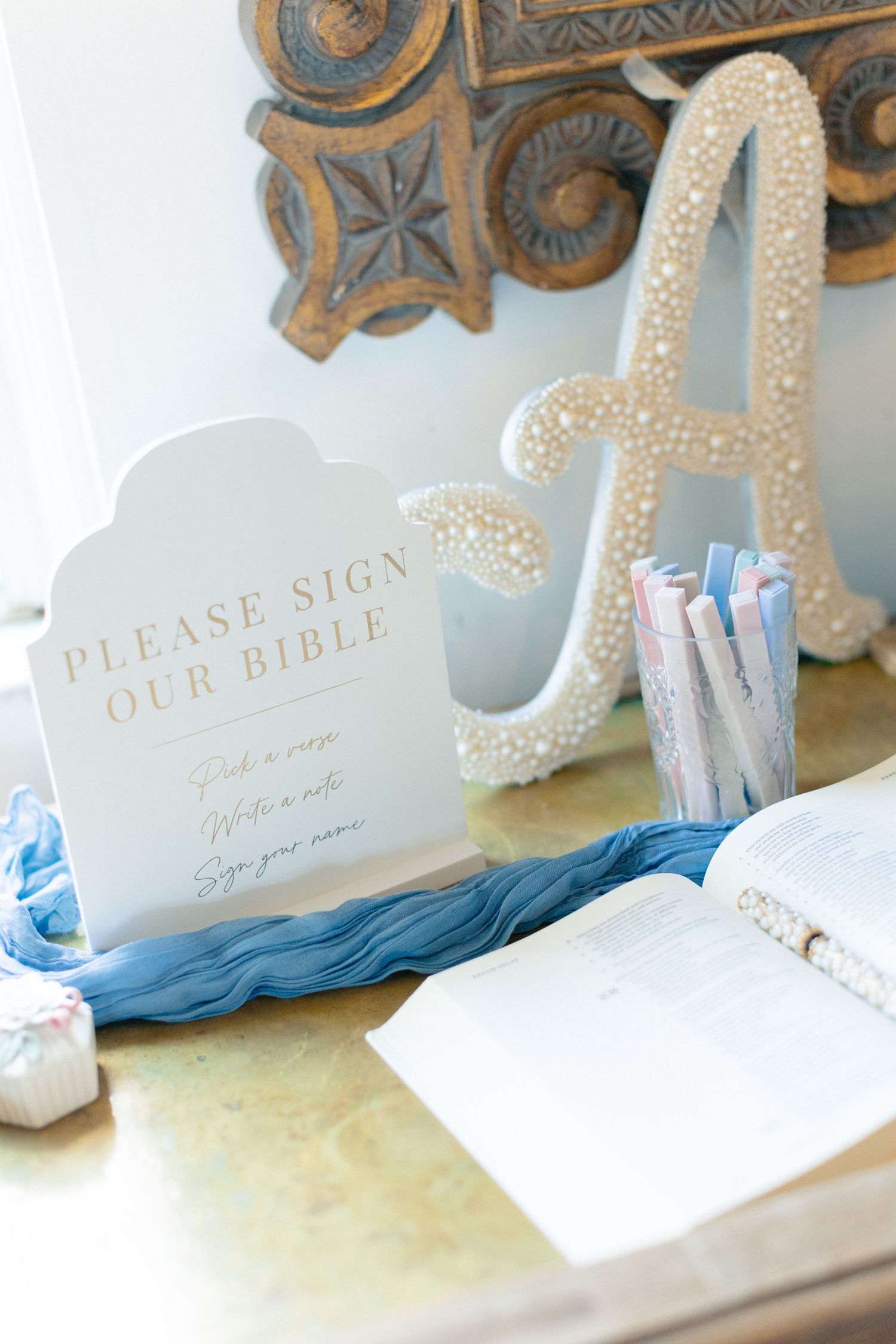 Wedding Bible signing station with pearl letter A, blue sign, and colorful pens at elegant ceremony reception table, wedding at Bella Cosa