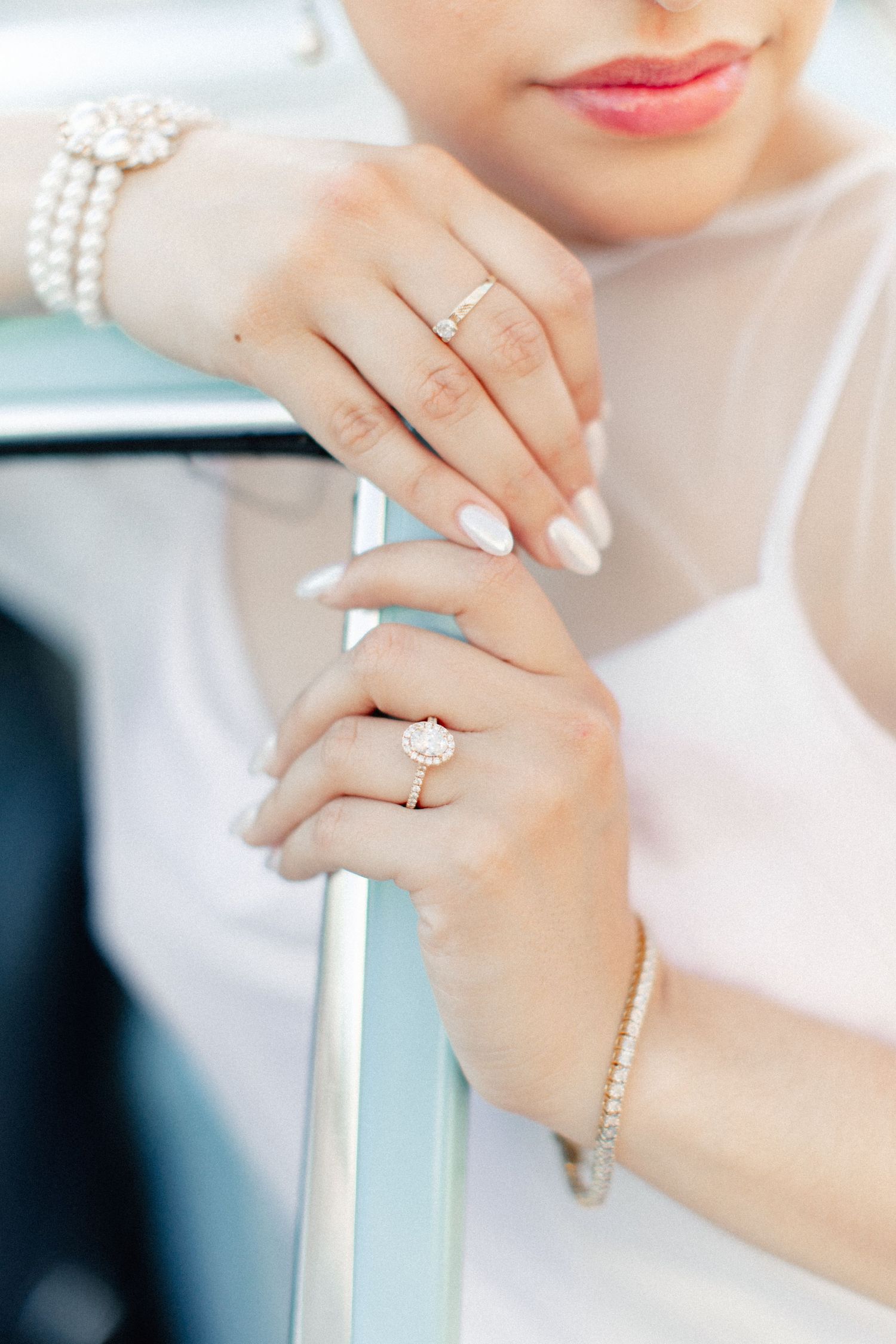 Close-up of bride's hands adorned with diamond engagement ring and pearl bracelet resting on a railing.