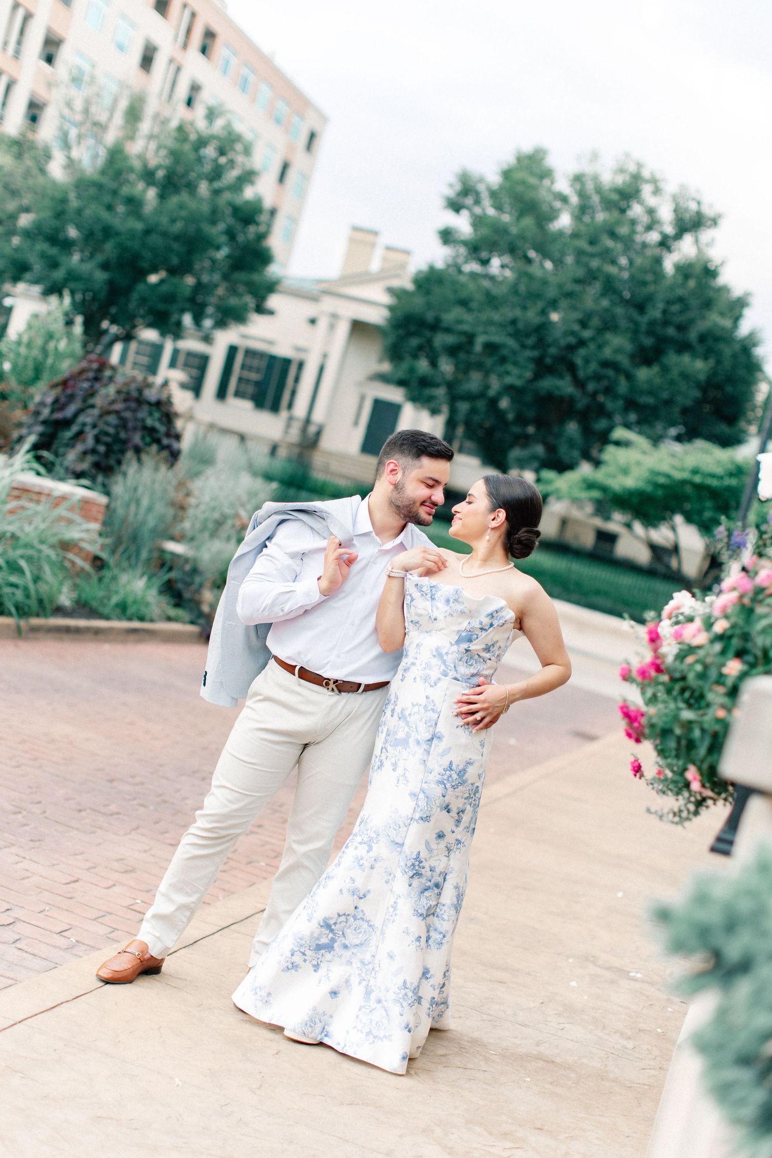 Couple in formal attire dancing outdoors, woman in floral blue dress, man in light gray suit.