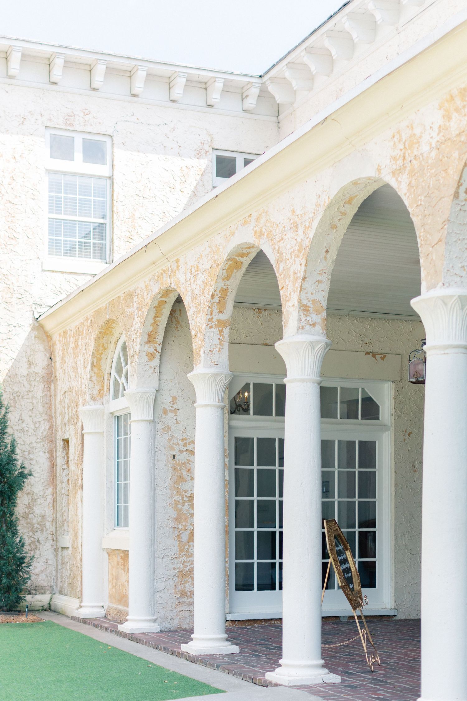 Elegant historic building with white arched colonnade, weathered stone walls, French doors, and brick pathway in soft natural light, Florida