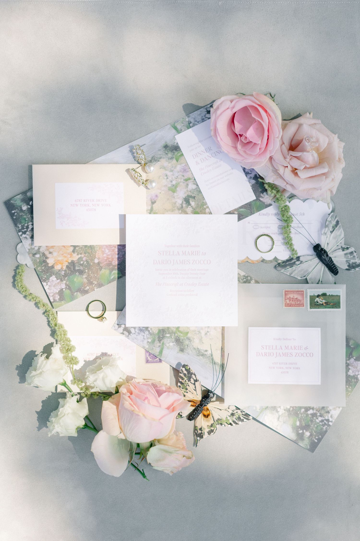 Romantic wedding invitation suite with watercolor floral envelopes, pink roses, butterfly, and gold rings flatlay.