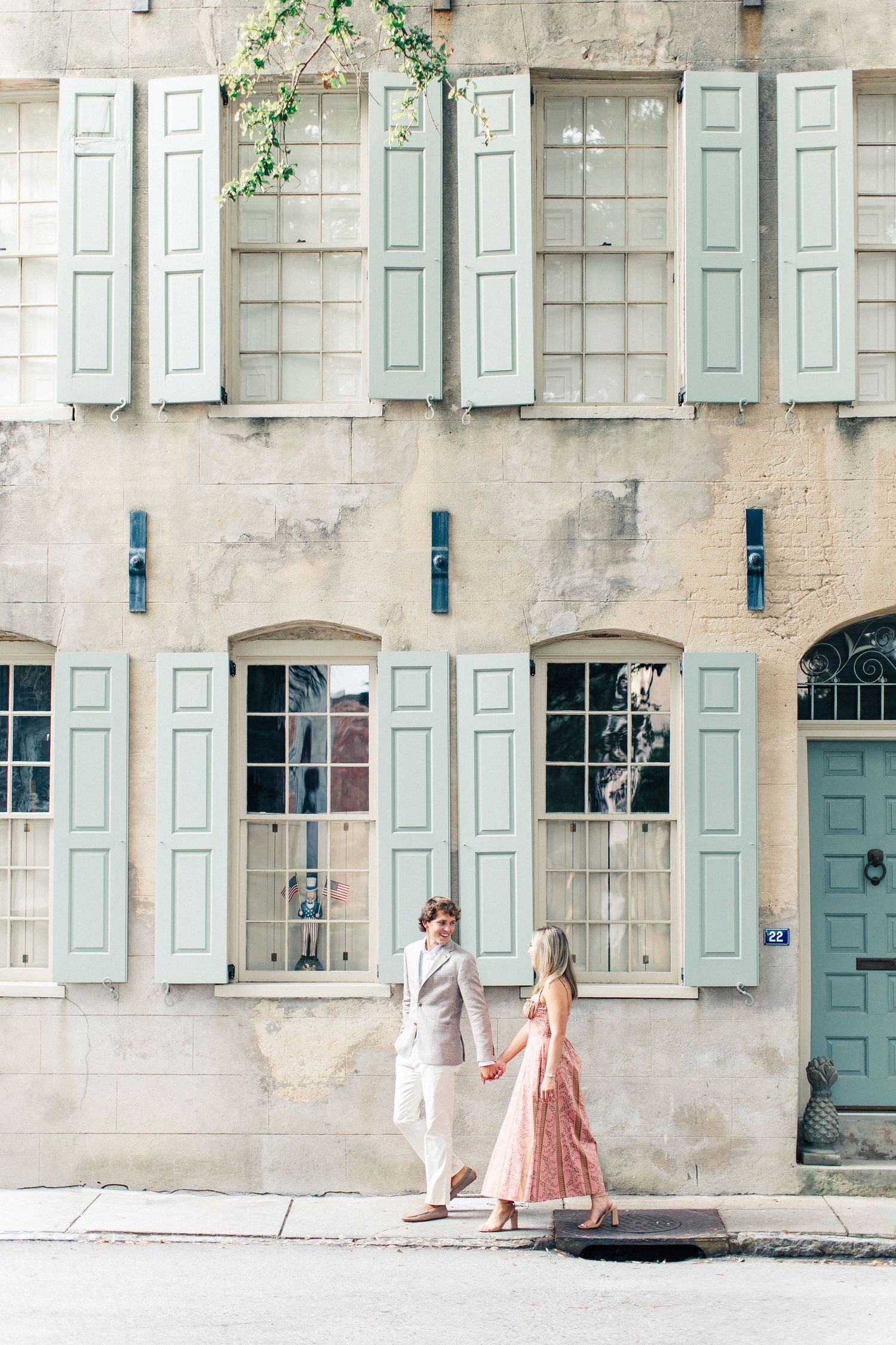 Couple holding hands in front of a charming building with mint green shutters in Charleston, SC.
