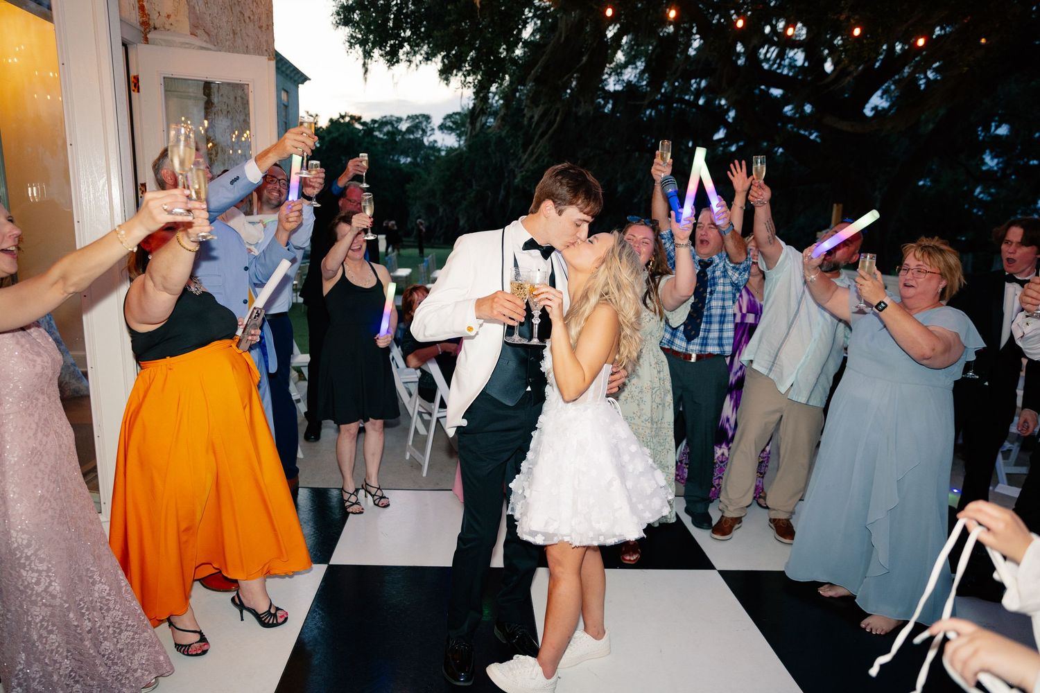 Newlyweds share a kiss on a checkered dance floor surrounded by cheering guests at an outdoor wedding reception, Florida