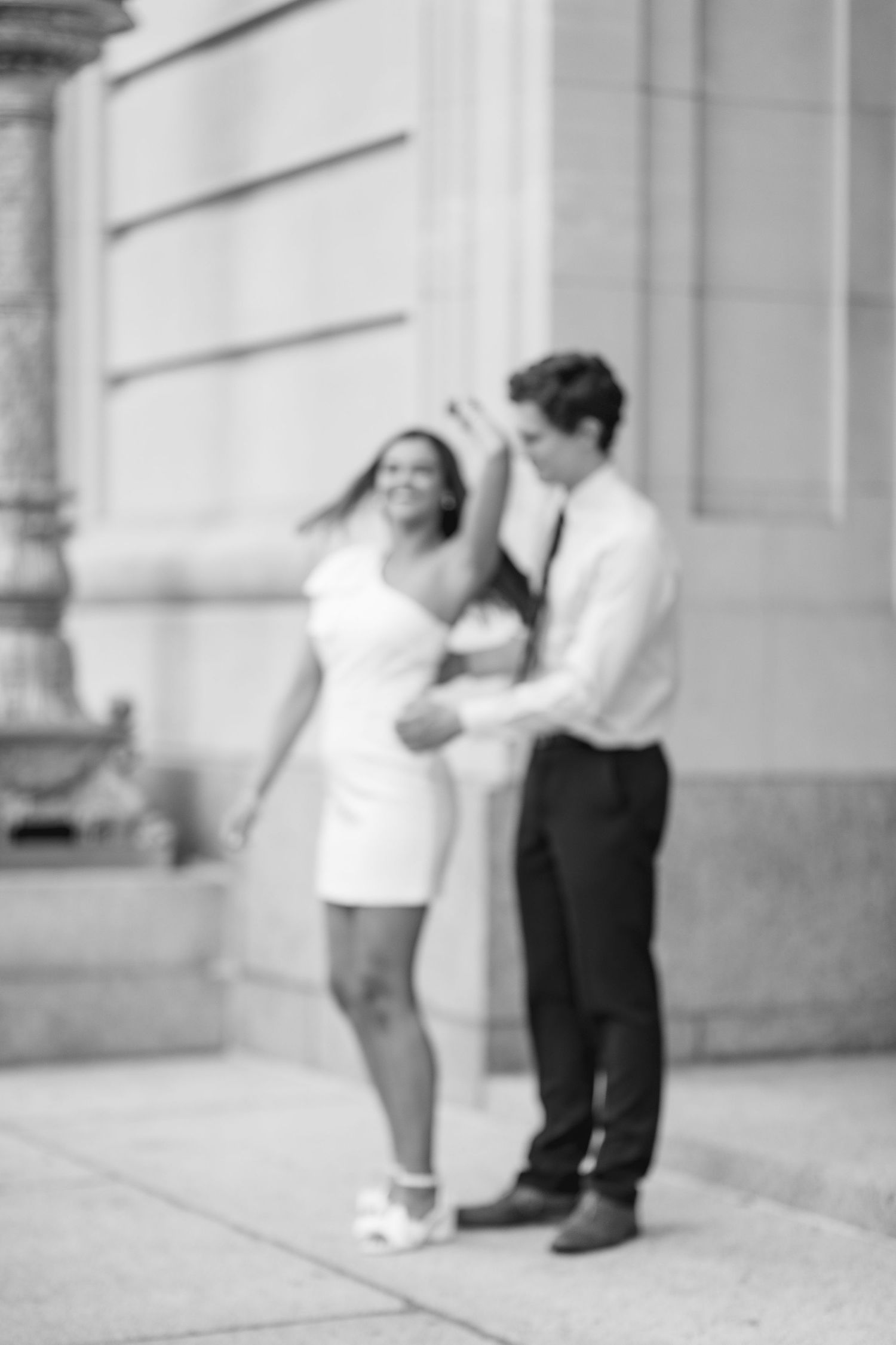 Black and white photo of couple dancing together outside a stone building.