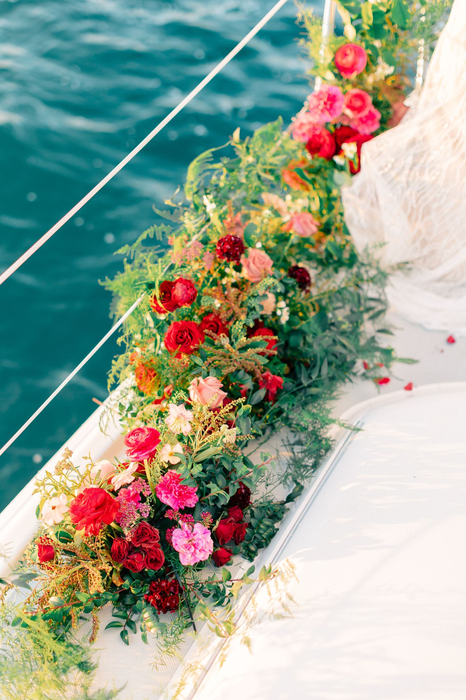 Lush red and pink floral garland decorating the side of a white yacht over turquoise water.