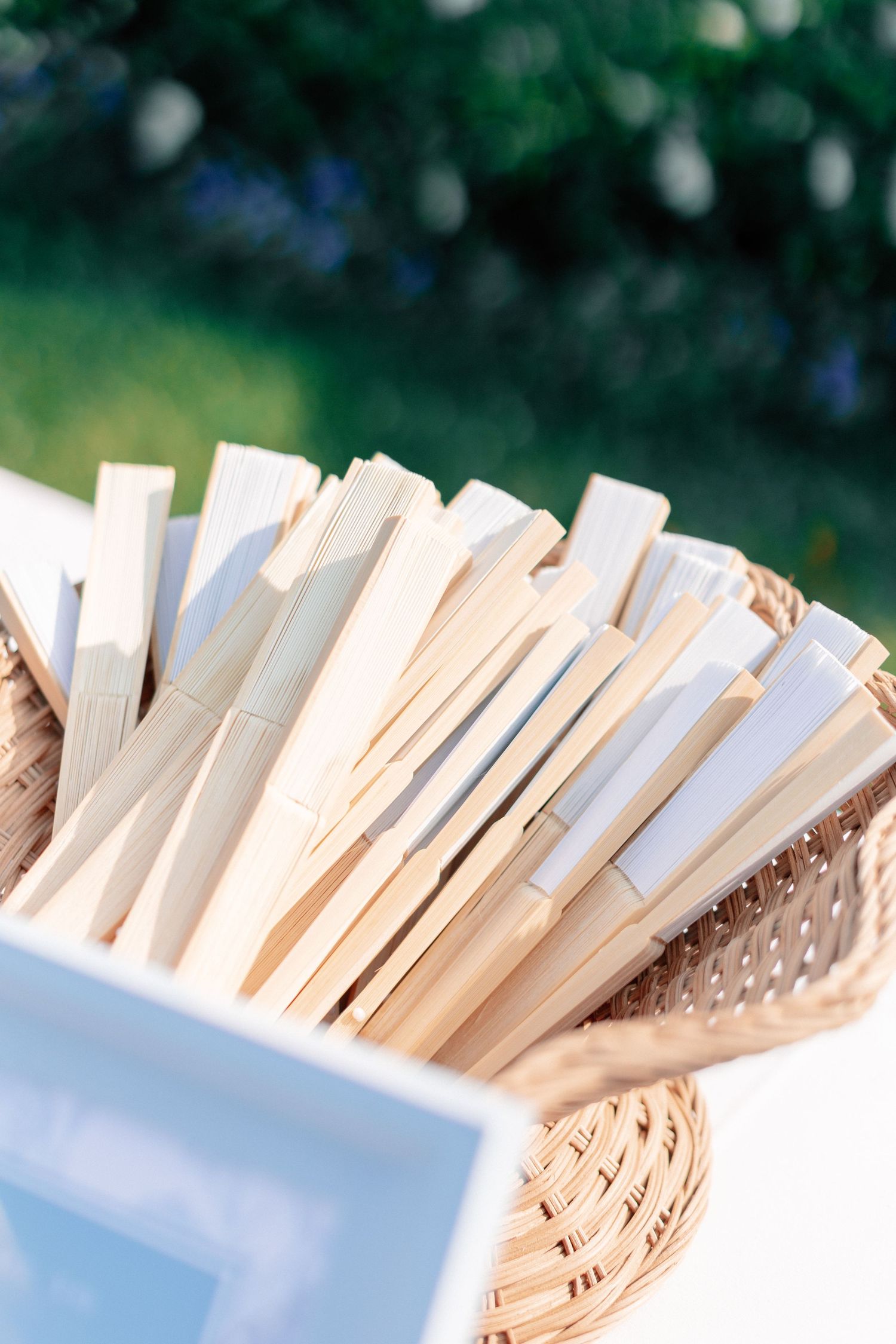 Wicker basket filled with wooden handheld folding fans for an outdoor wedding ceremony.