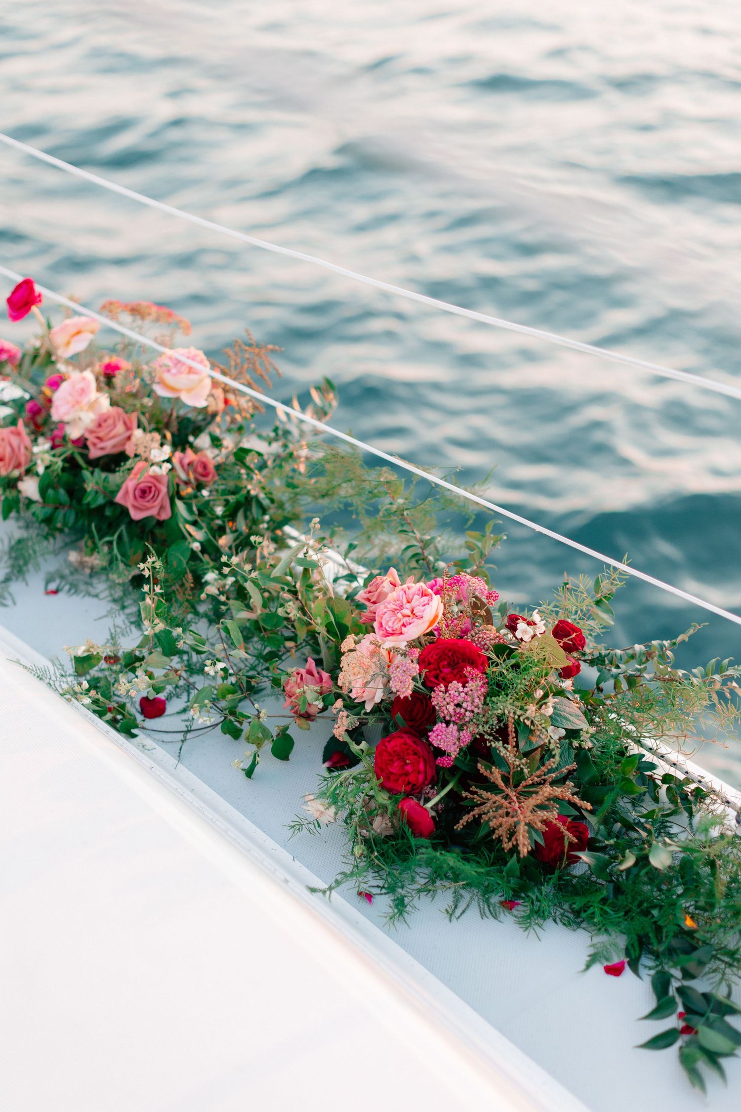 Lush pink and red floral arrangement with greenery decorating the side of a white yacht over blue ocean water.