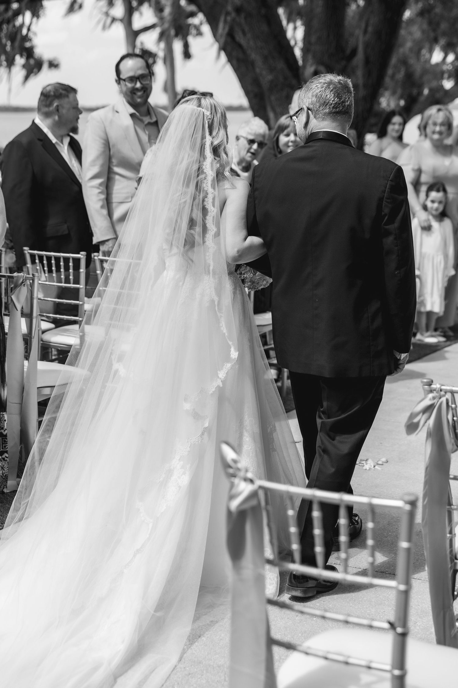 Black and white photo of a bride walking down the aisle with her father at an outdoor wedding ceremony, wedding at Bella Cosa