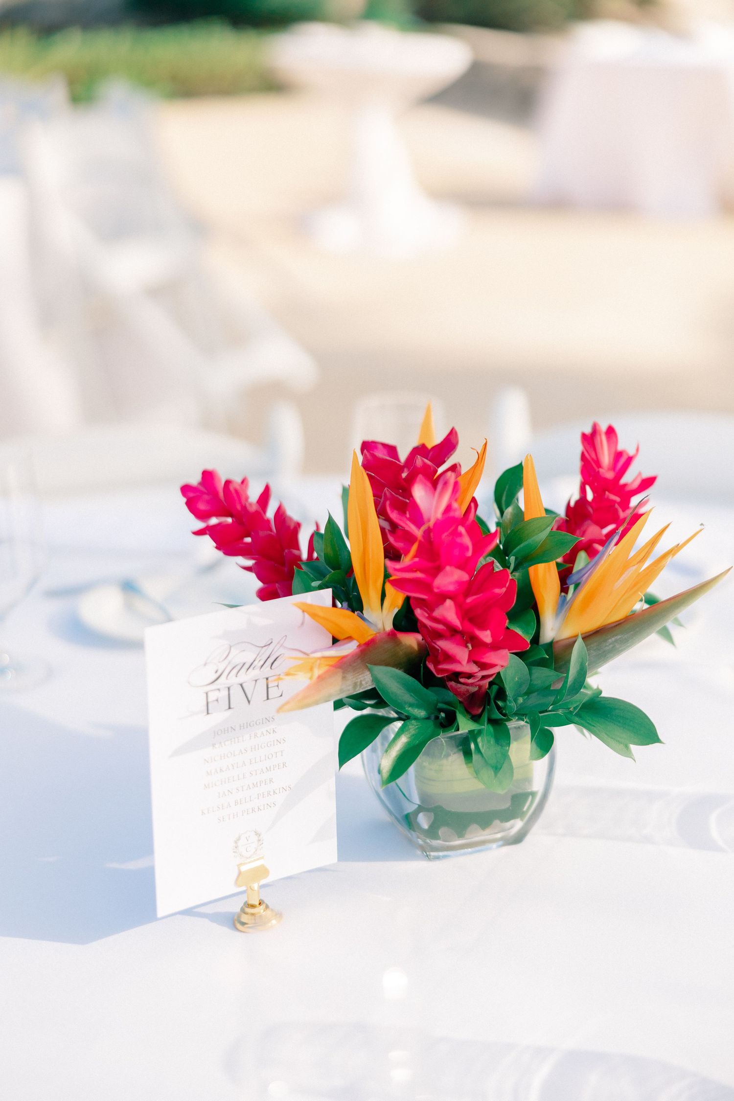 Tropical wedding centerpiece with birds of paradise and pink ginger flowers in a glass vase beside a Table Five sign.