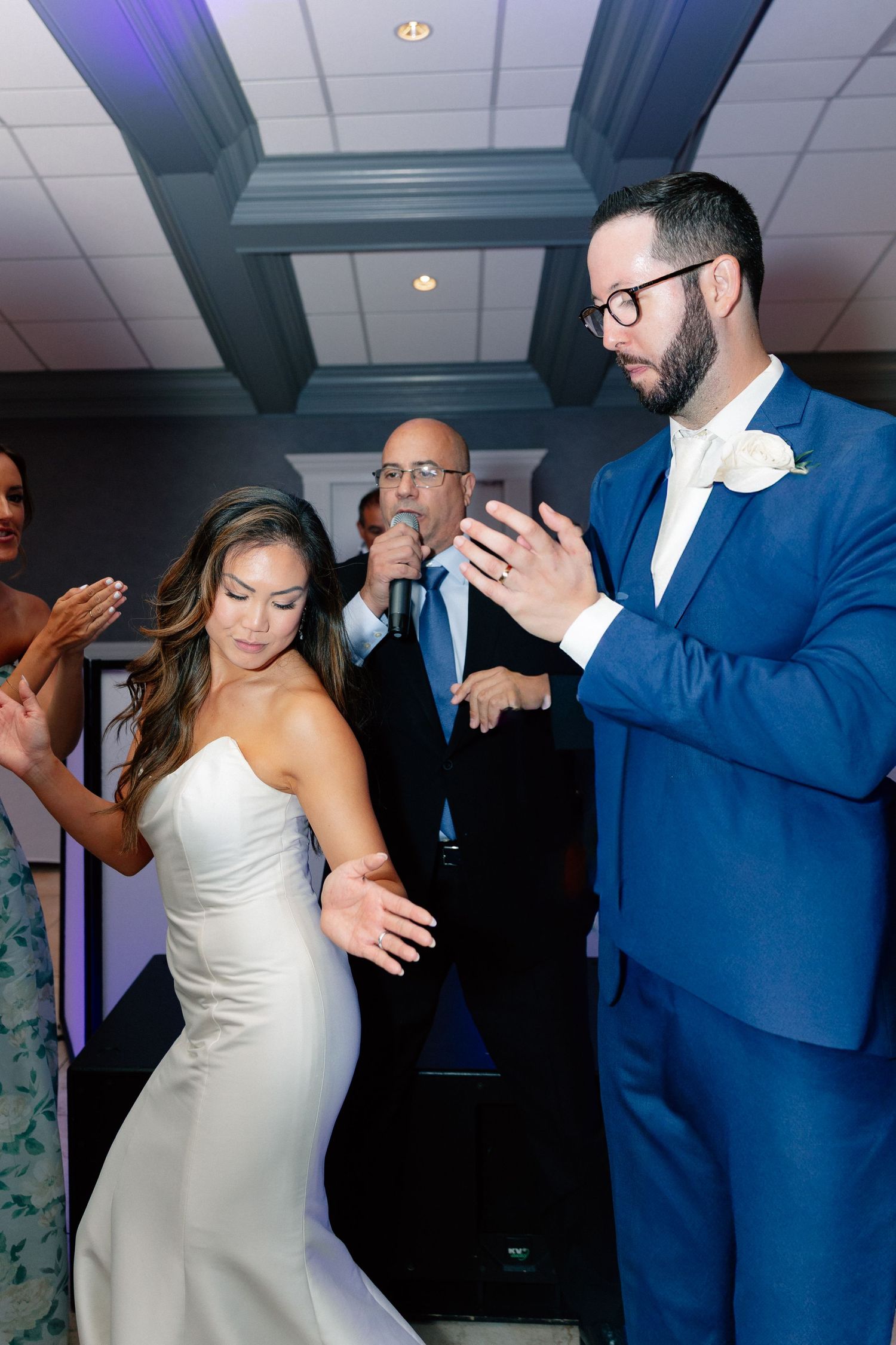 Bride in white gown and groom in blue suit share first dance at elegant wedding reception.