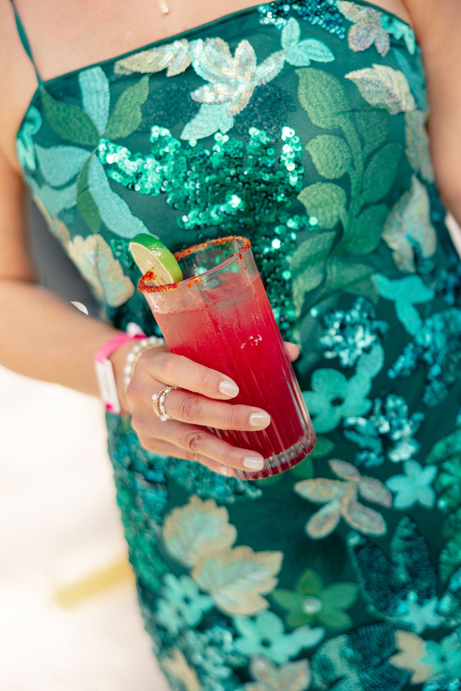 Woman in green sequin floral dress holding a red cocktail with lime garnish and salted rim at a party.