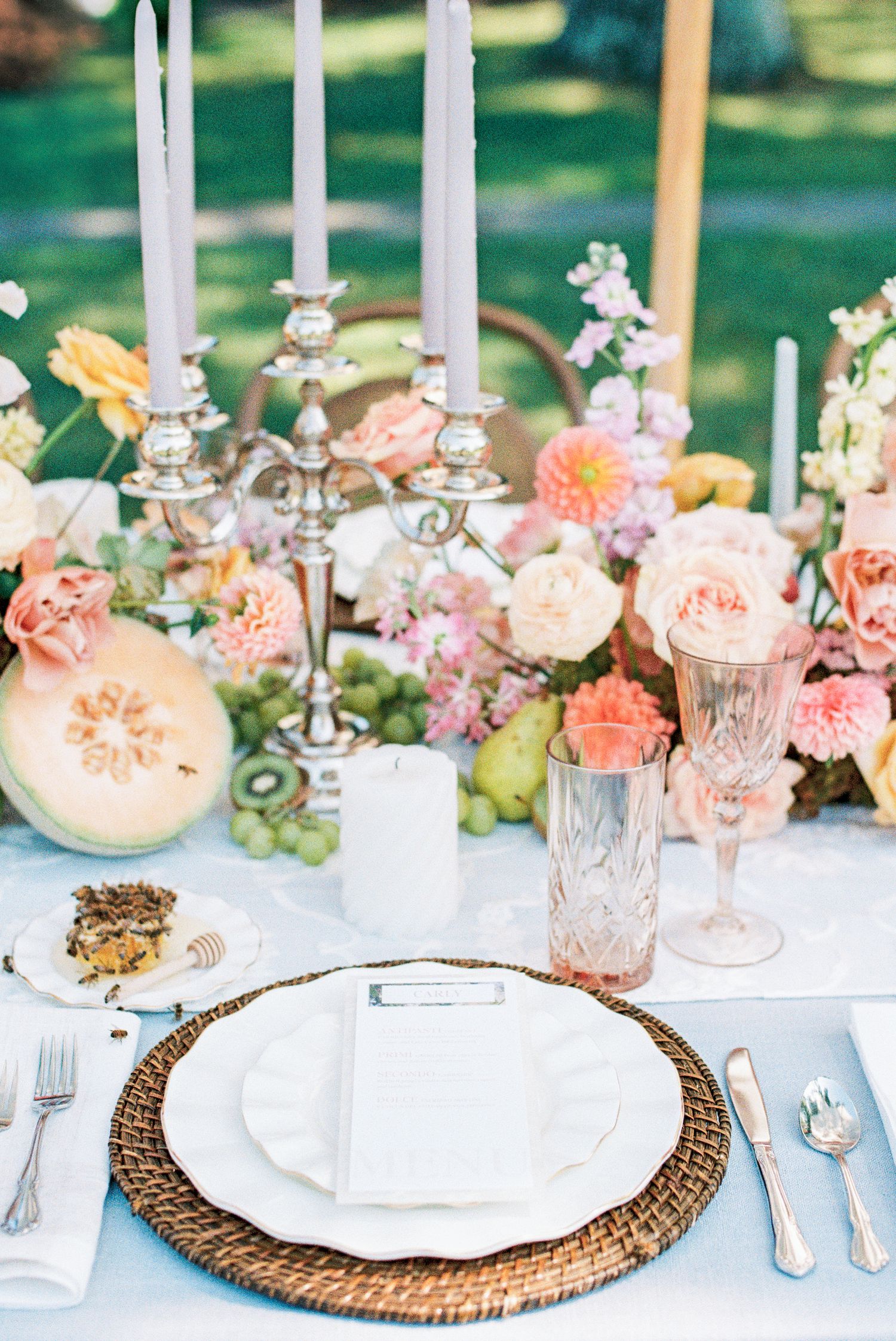 Elegant outdoor wedding tablescape with pastel florals, silver candelabra, wicker charger plates, and pink glassware.