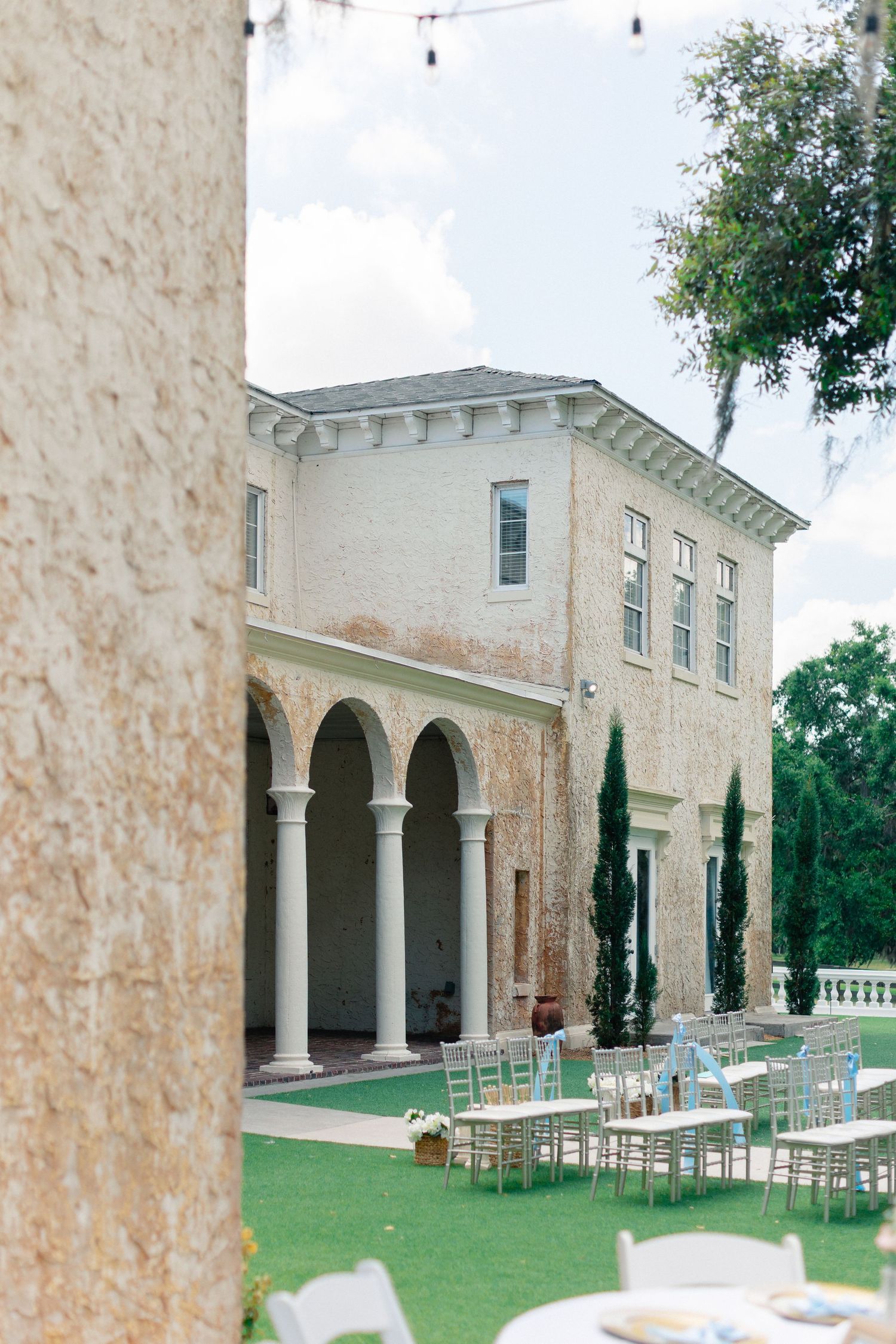 Elegant Italian-style villa wedding venue with arched colonnade, cypress trees, and outdoor reception seating on manicured lawn, Florida