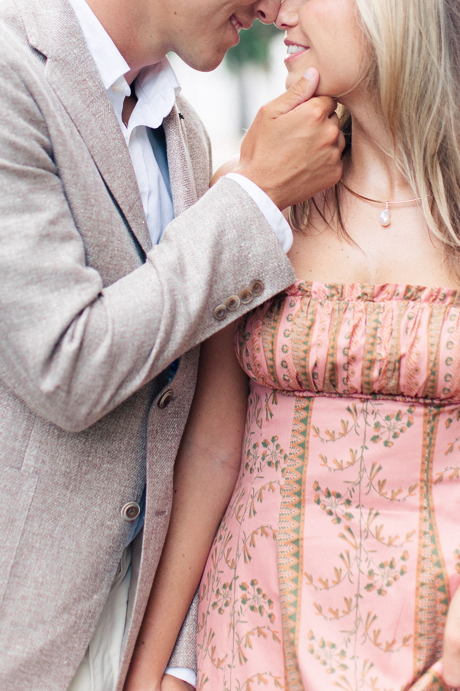 Romantic couple in elegant attire sharing an intimate moment, man in gray blazer gently touching blonde woman's face.