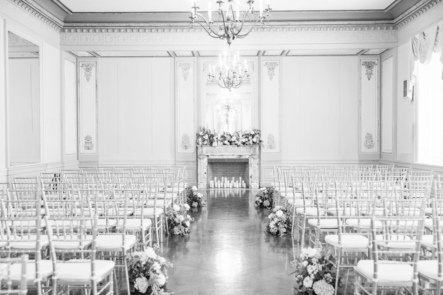 Elegant black and white wedding ceremony setup with chiavari chairs, floral arrangements, and chandelier in a grand ballroom.