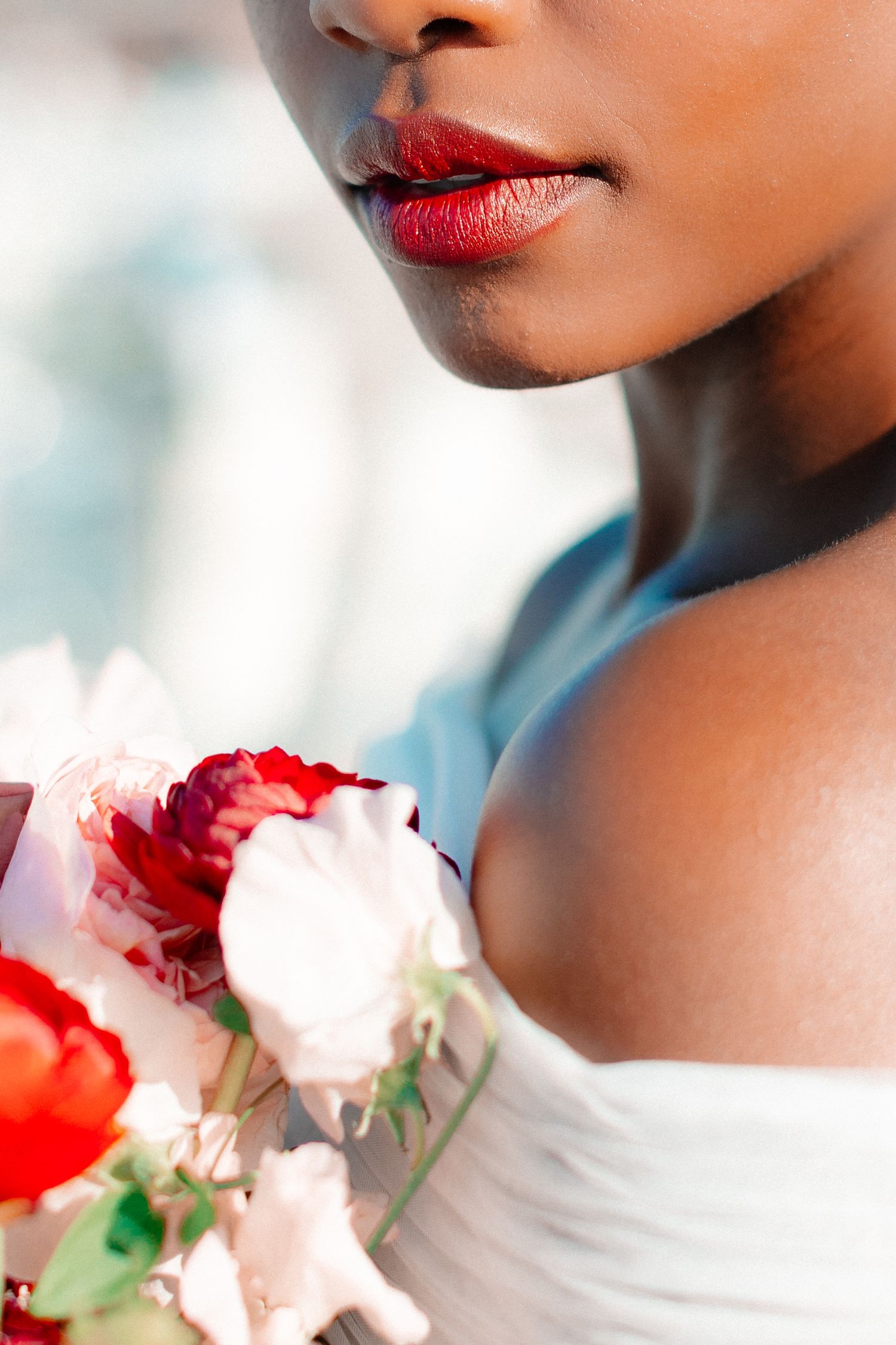 Close-up of a bride with red lips holding a bouquet of red and pink roses in a white dress.