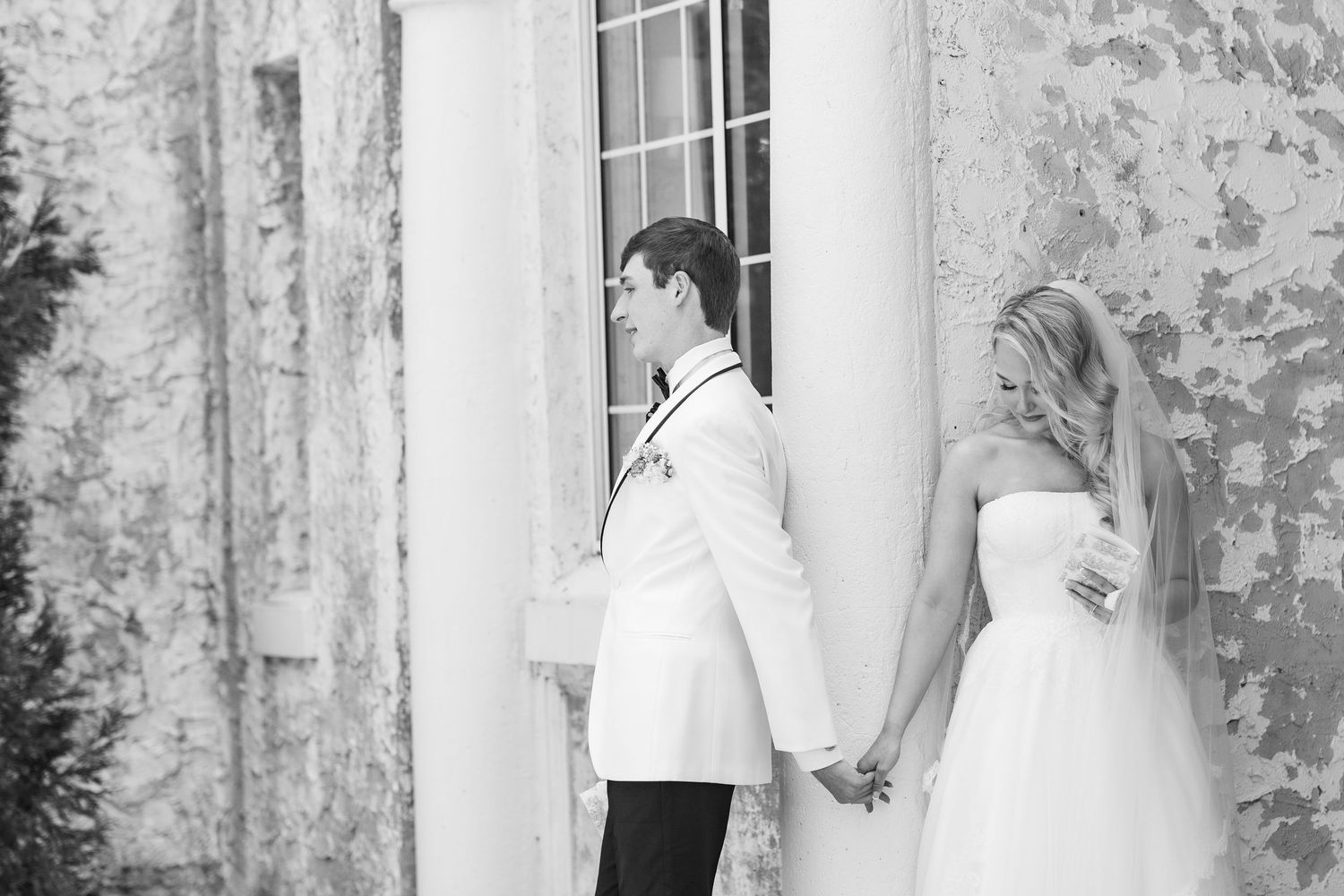 Black and white photo of a bride and groom holding hands outside a historic building with columns, wedding at Bella Cosa