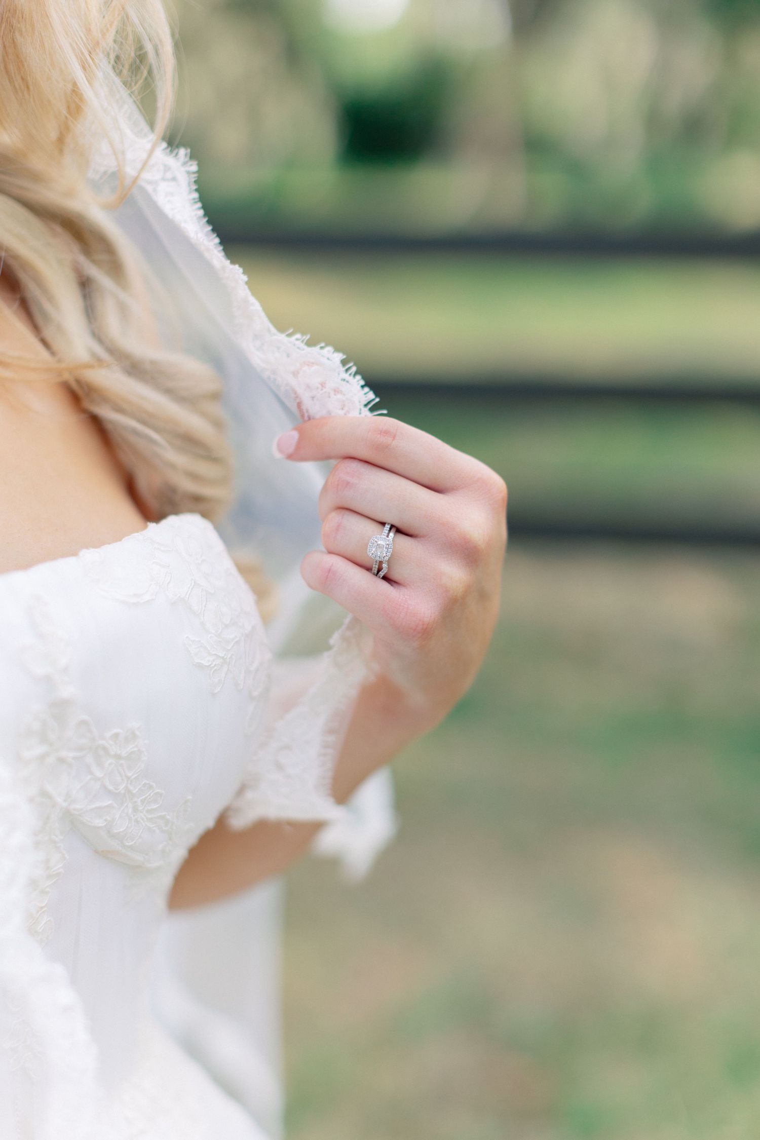 Bride in white lace wedding dress holding veil, showcasing diamond engagement ring and wedding band on her finger. wedding at Bella Cosa