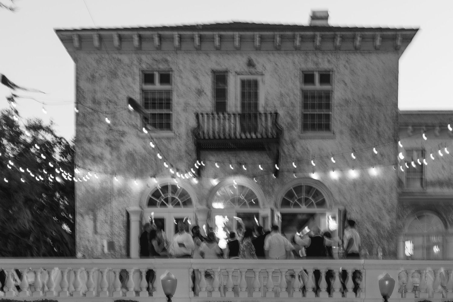 Black and white photo of a historic stone venue with string lights at dusk.