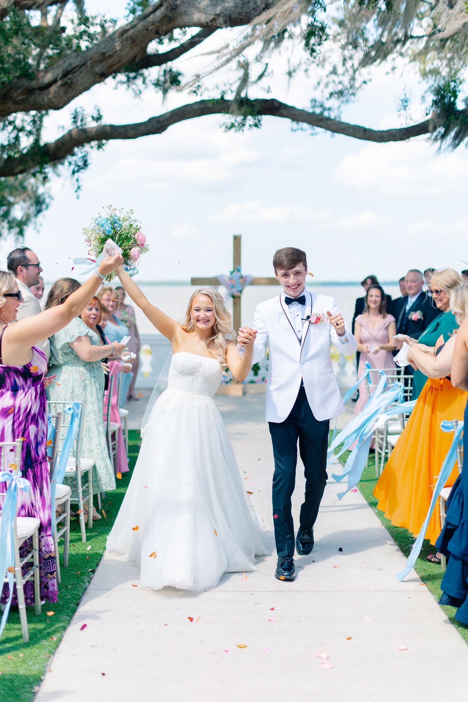 Joyful bride and groom walk down outdoor aisle after wedding ceremony, guests cheering with colorful ribbons and confetti, Florida