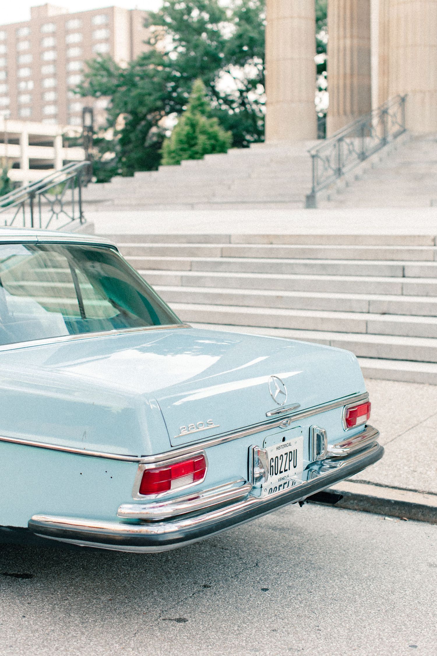 Rear view of classic vintage light blue Mercedes-Benz parked in front of neoclassical building with stone steps.