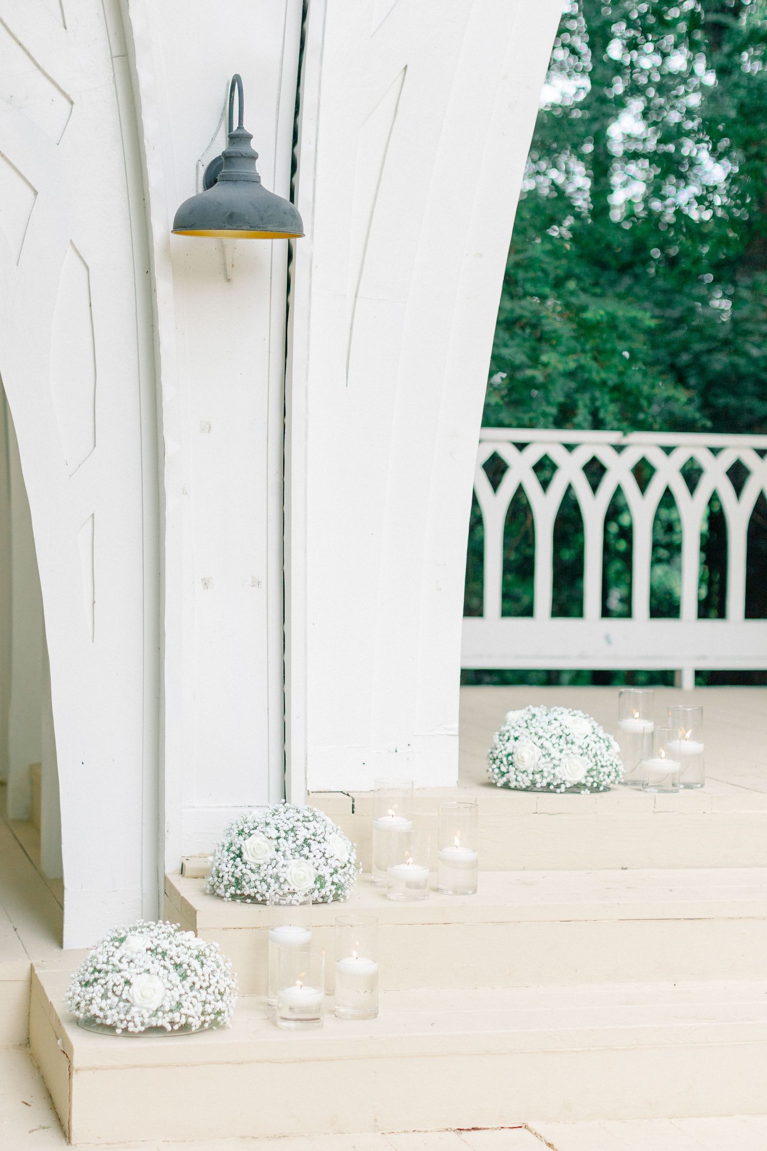 White chapel steps adorned with baby's breath floral arrangements and glass candle holders for an elegant wedding ceremony.