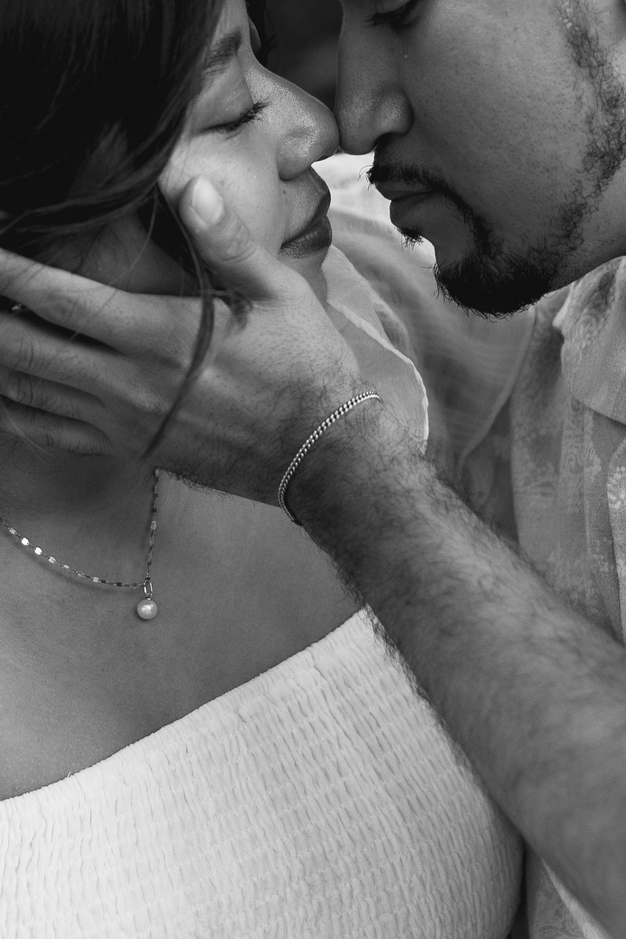 A close black and white portrait of a couple nearly kissing, the mans hand tenderly cradling the womans face.