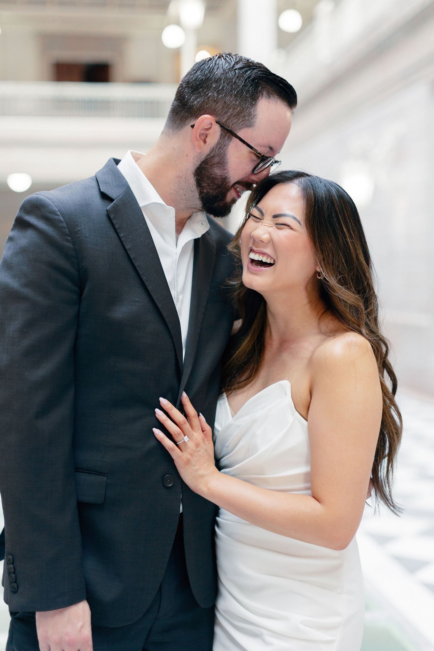 Couple laughing together during engagement session inside elegant white building.