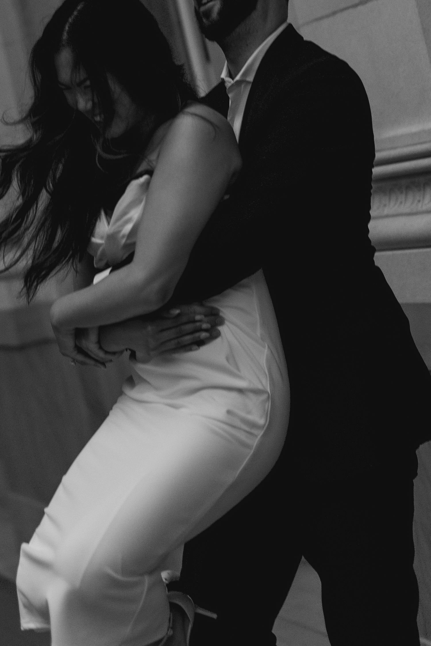Black and white photo of an elegant couple embracing, woman in white dress and man in dark suit.