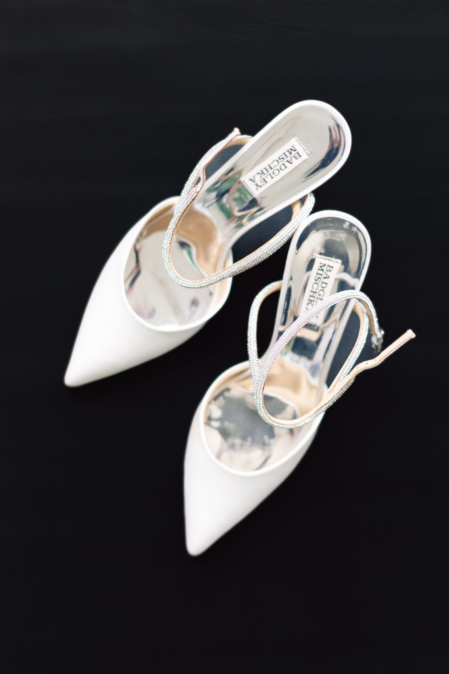 Elegant white pointed-toe slingback heels by Badgley Mischka displayed on a black background, perfect for a bride.