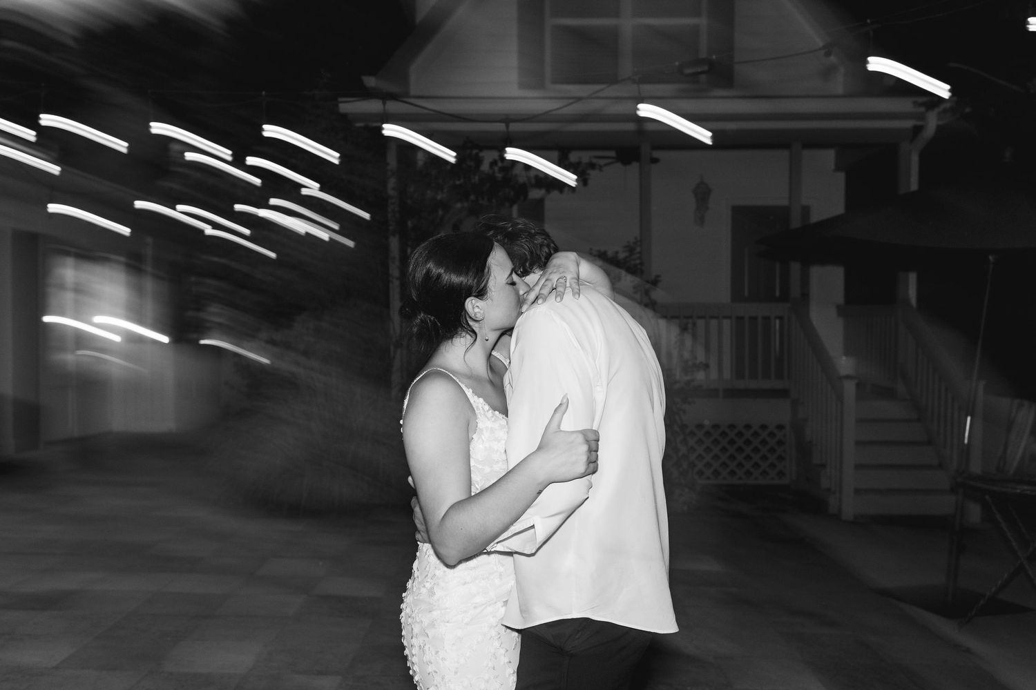 Black and white photo of a couple sharing a romantic kiss during their wedding reception outdoors at night.