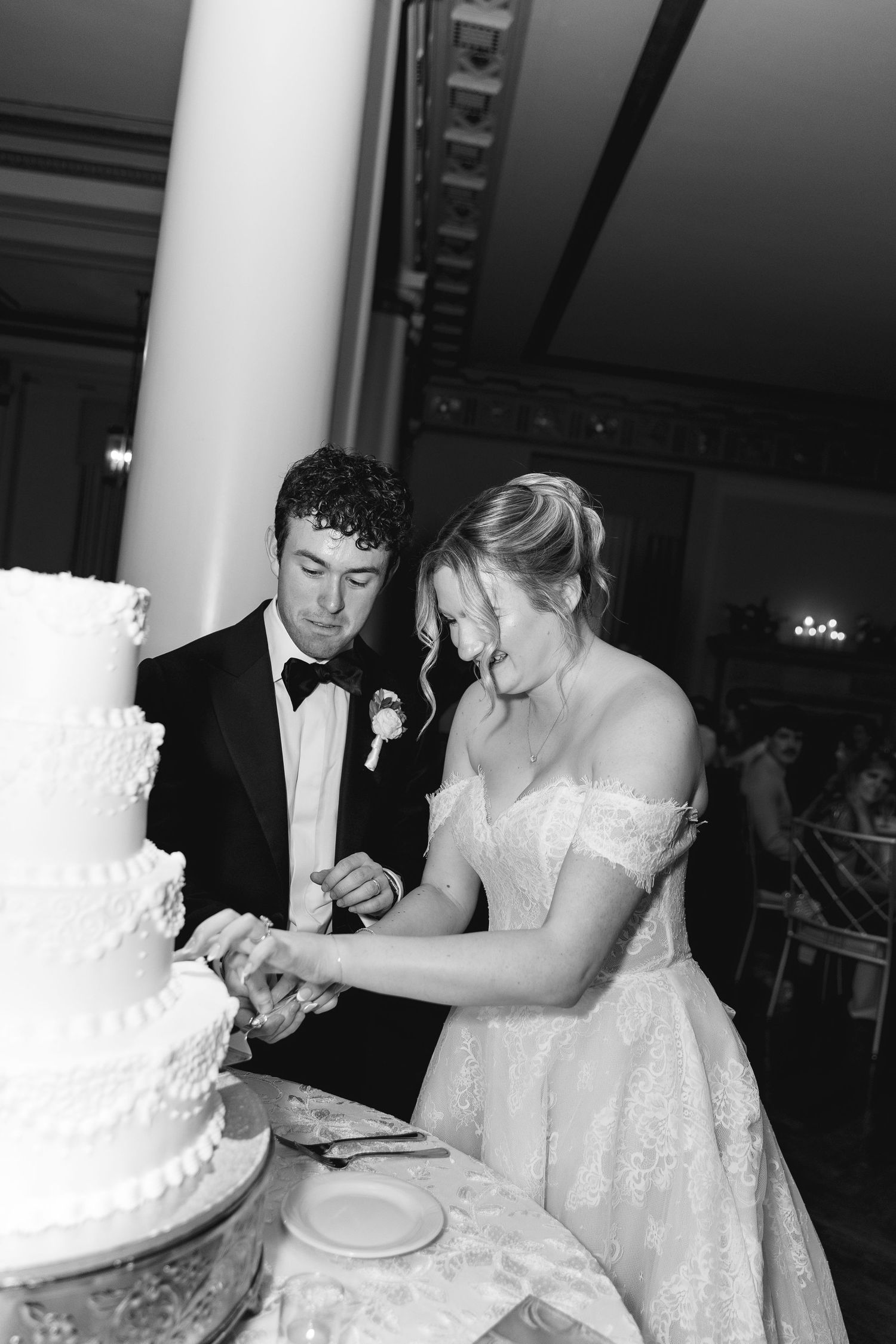 Bride and groom cutting their white tiered wedding cake together in a black and white photo at their reception.