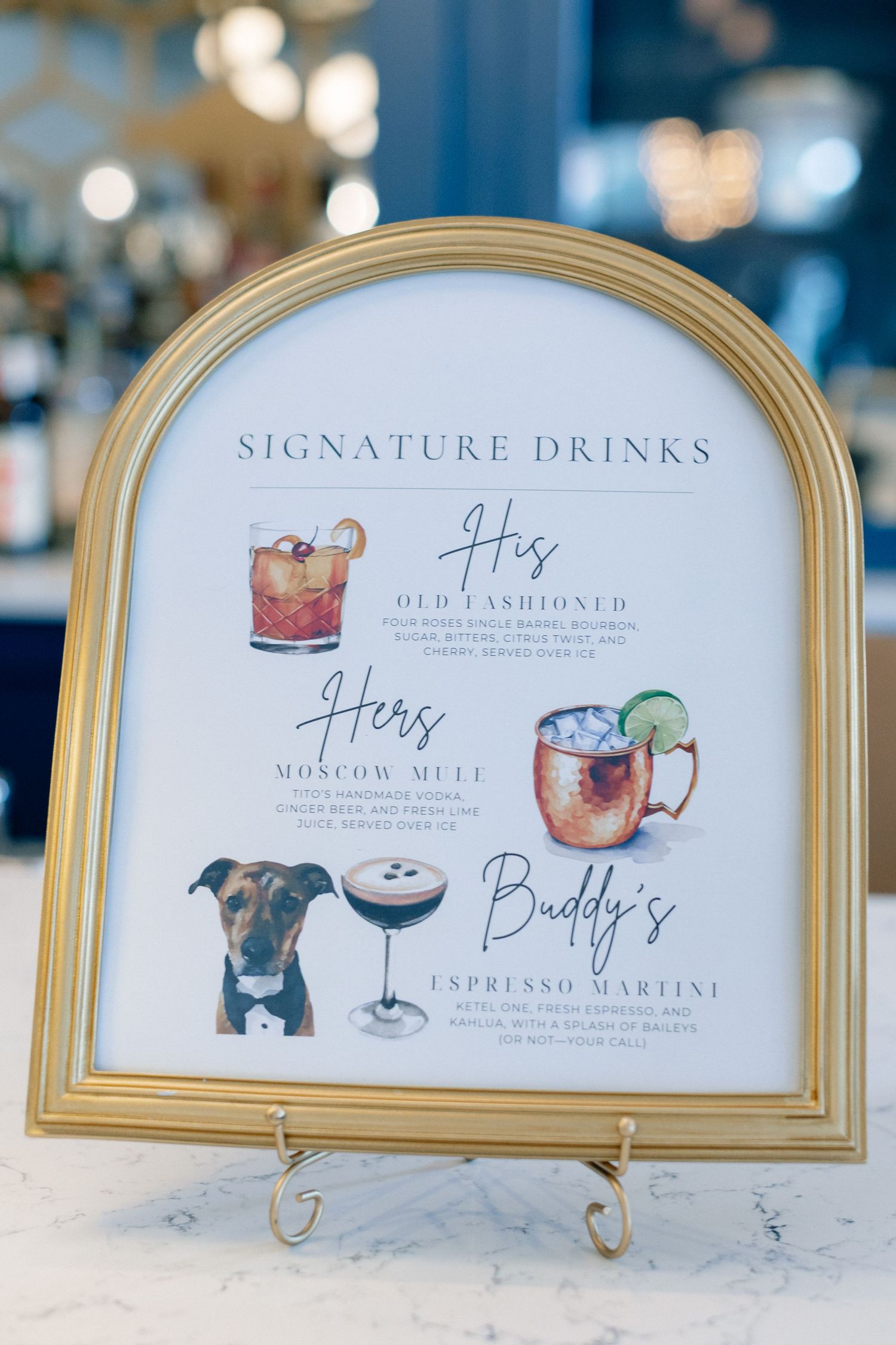 Gold framed signature drinks menu sign featuring His, Hers, and Buddy's cocktail selections at a wedding reception.