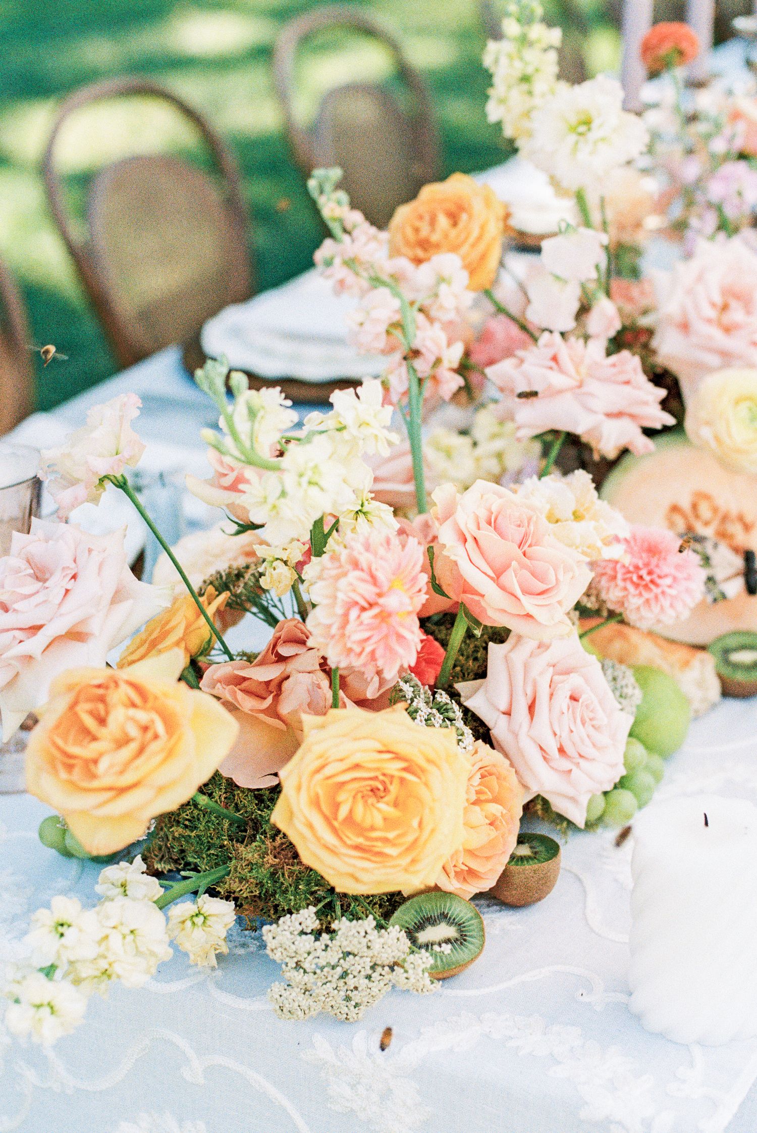Elegant wedding table centerpiece with peach and pink roses, white blooms, and greenery on a light blue tablecloth.