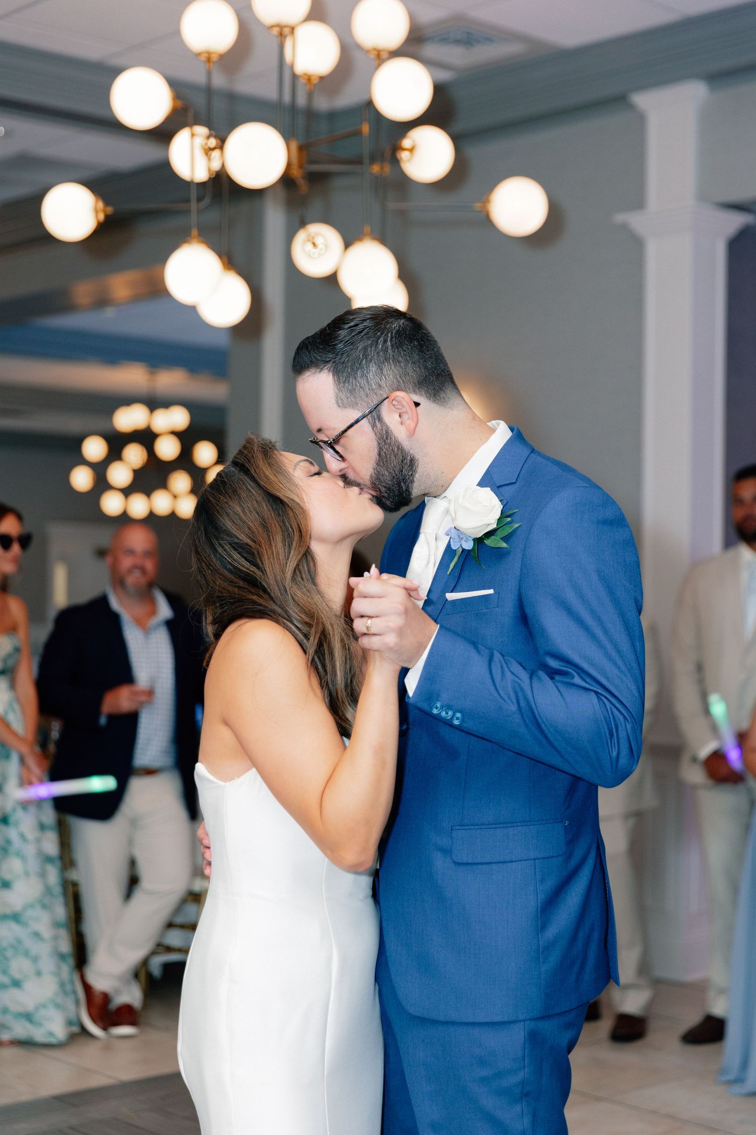 Bride and groom share first dance kiss in elegant venue with globe chandelier lighting during wedding reception.