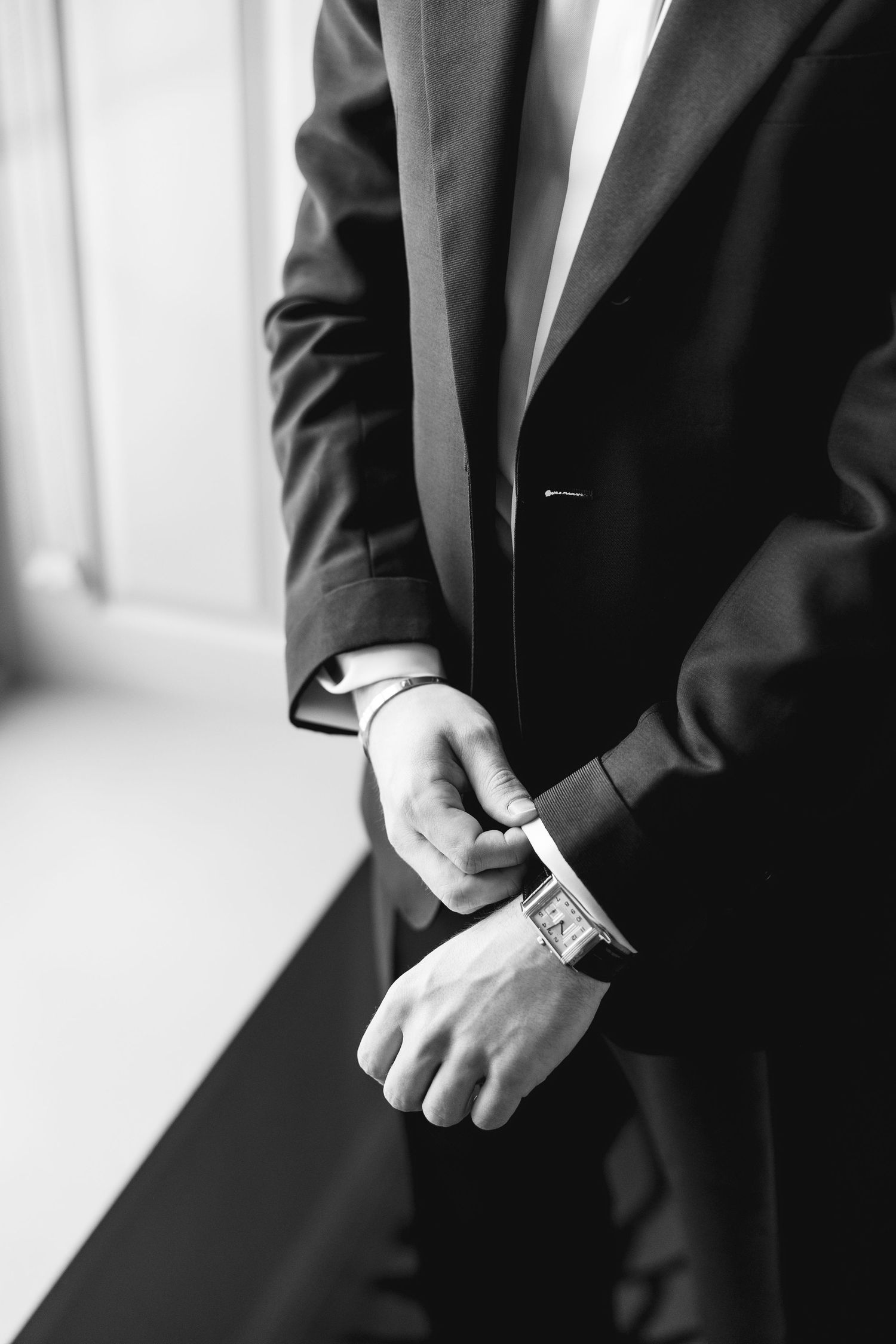 Black and white photo of a man in a suit adjusting his cufflinks, wearing a square-faced wristwatch.