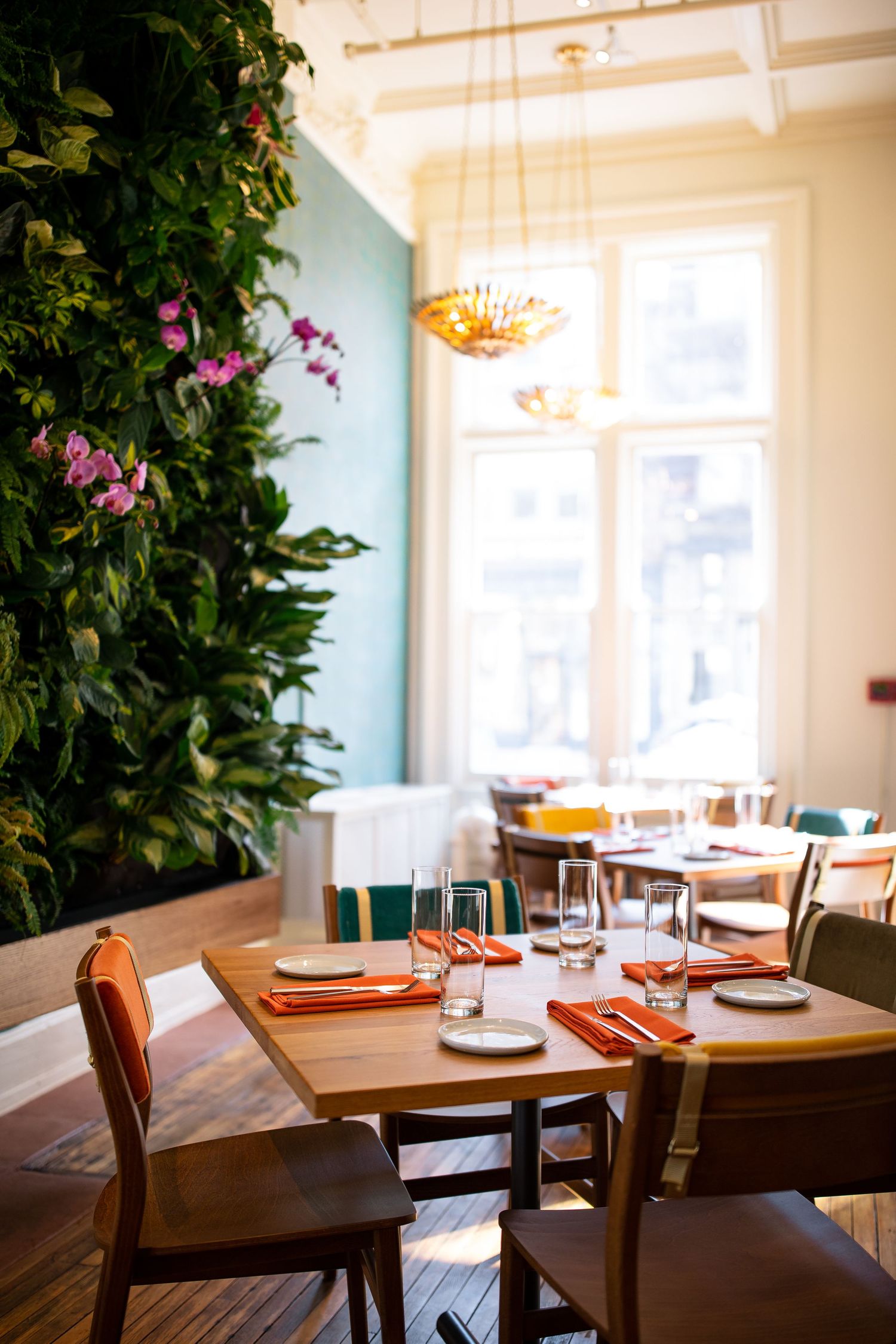 Elegant restaurant dining area with living green wall, wooden tables set with orange napkins, and warm pendant lighting.