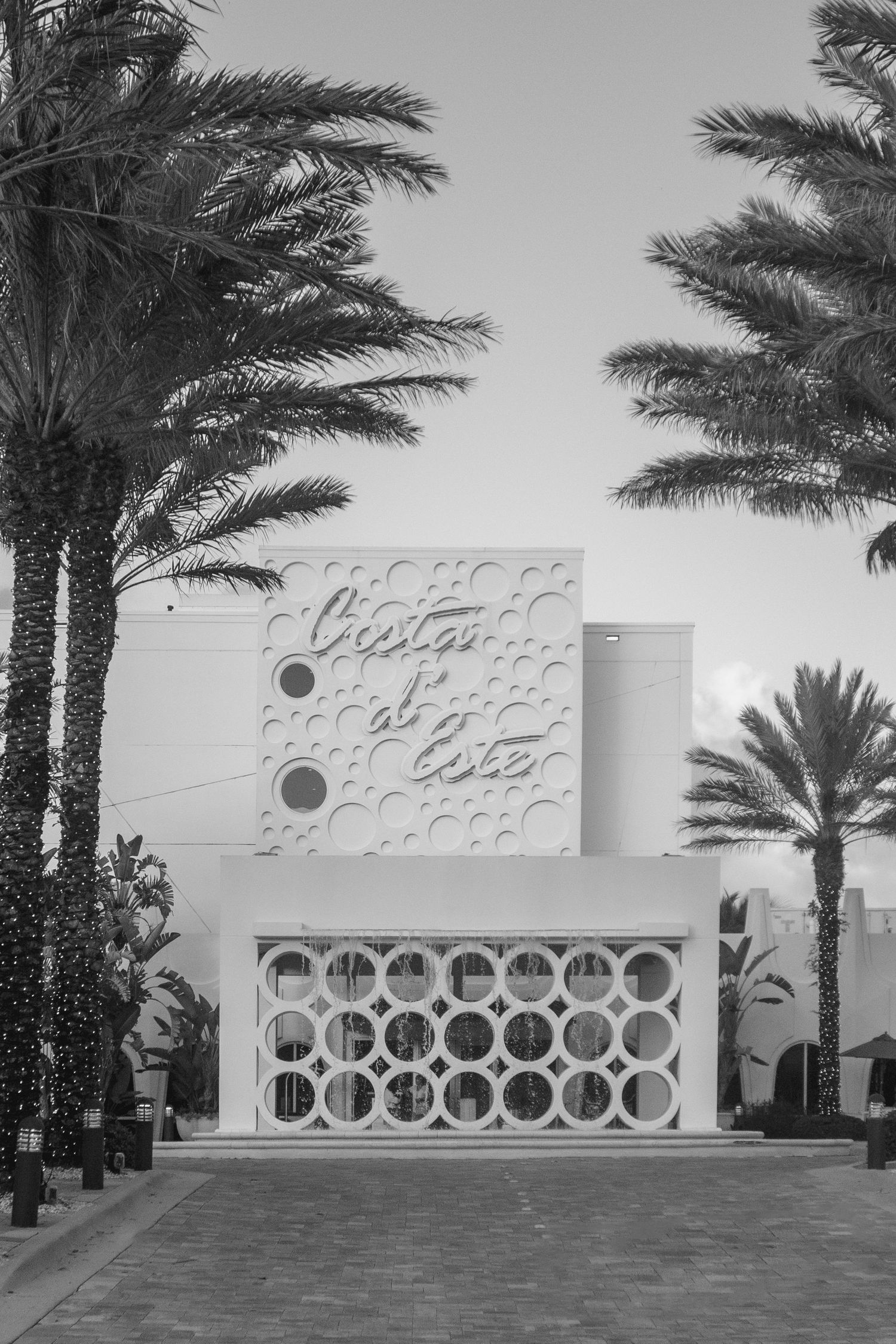 Black and white photo of Costa del Este building facade with decorative circular patterns, flanked by tall palm trees.