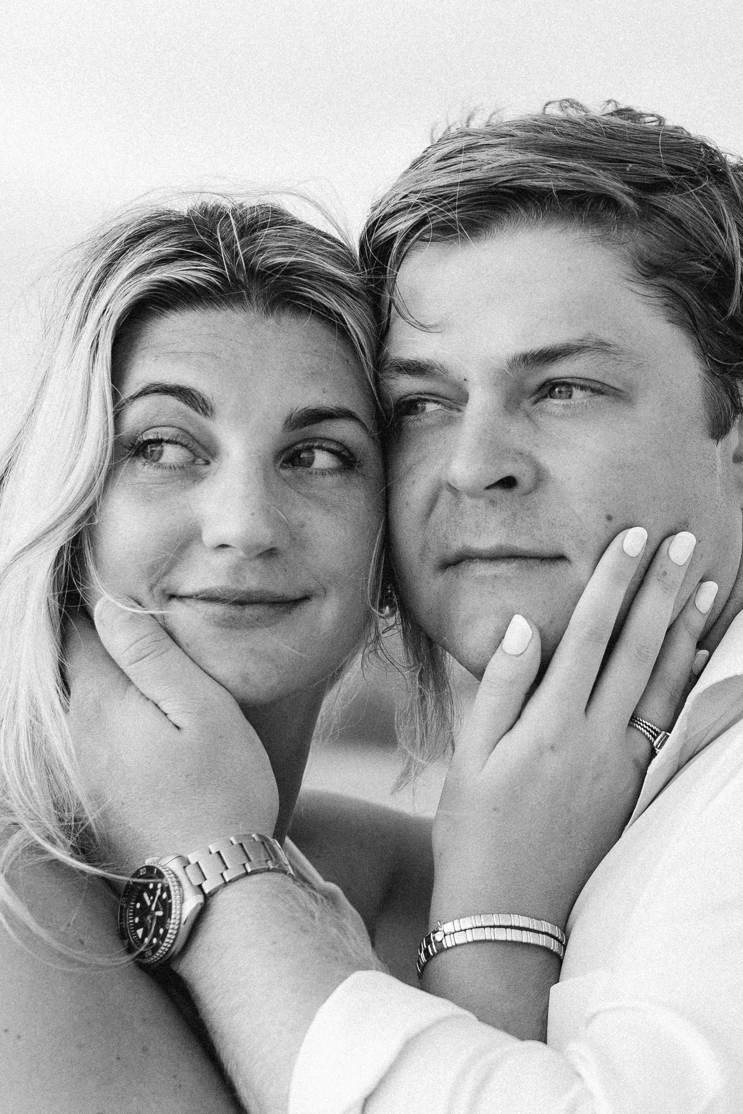 Black and white photo of a smiling couple cheek to cheek, woman wearing a watch, man in white shirt.