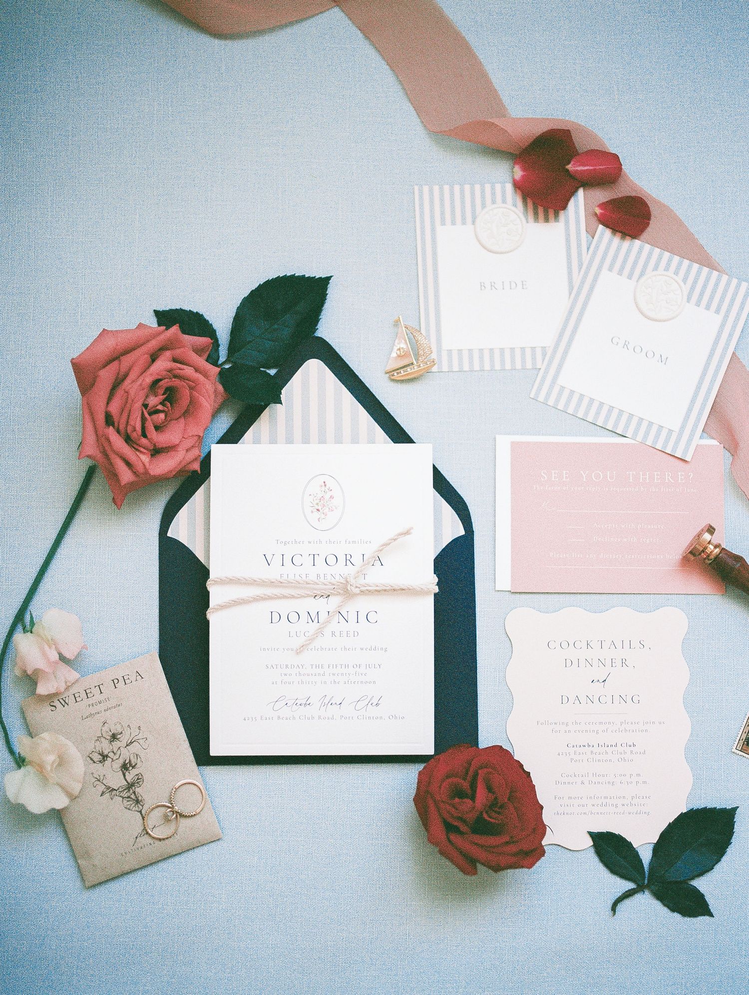 Elegant wedding invitation suite with striped envelopes, red roses, and pink accents on a soft blue background.
