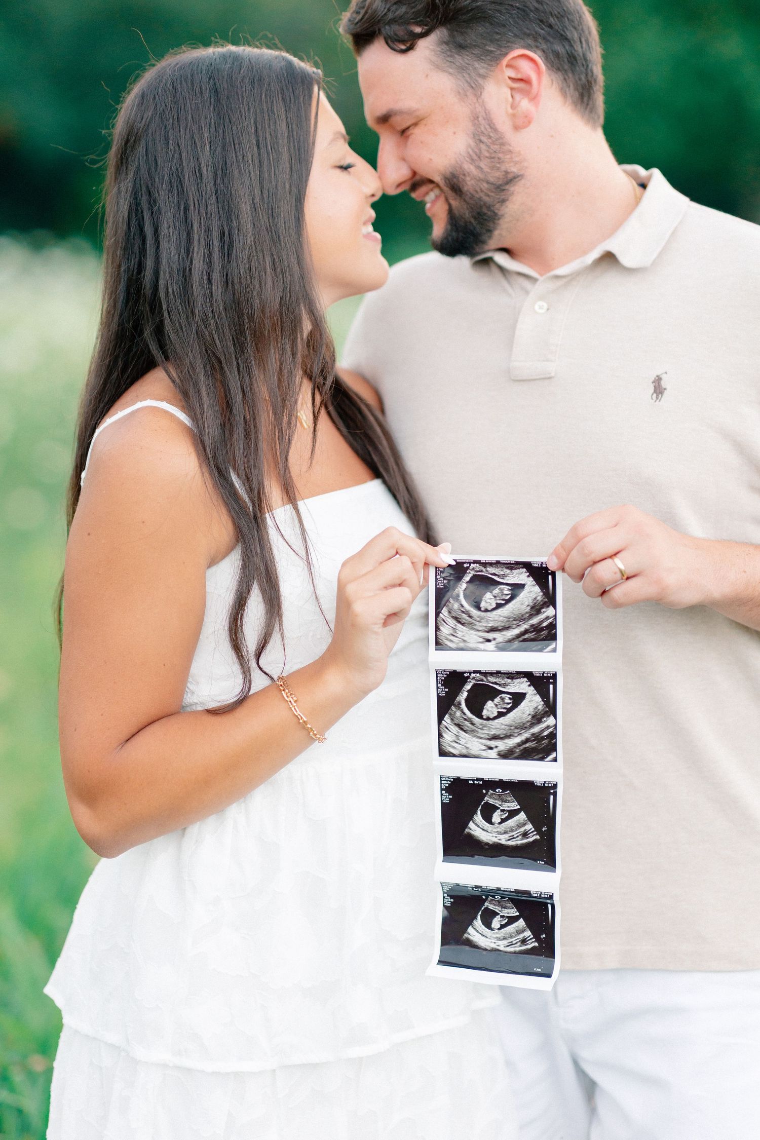Couple sharing a tender moment while holding ultrasound photos outdoors, announcing pregnancy.